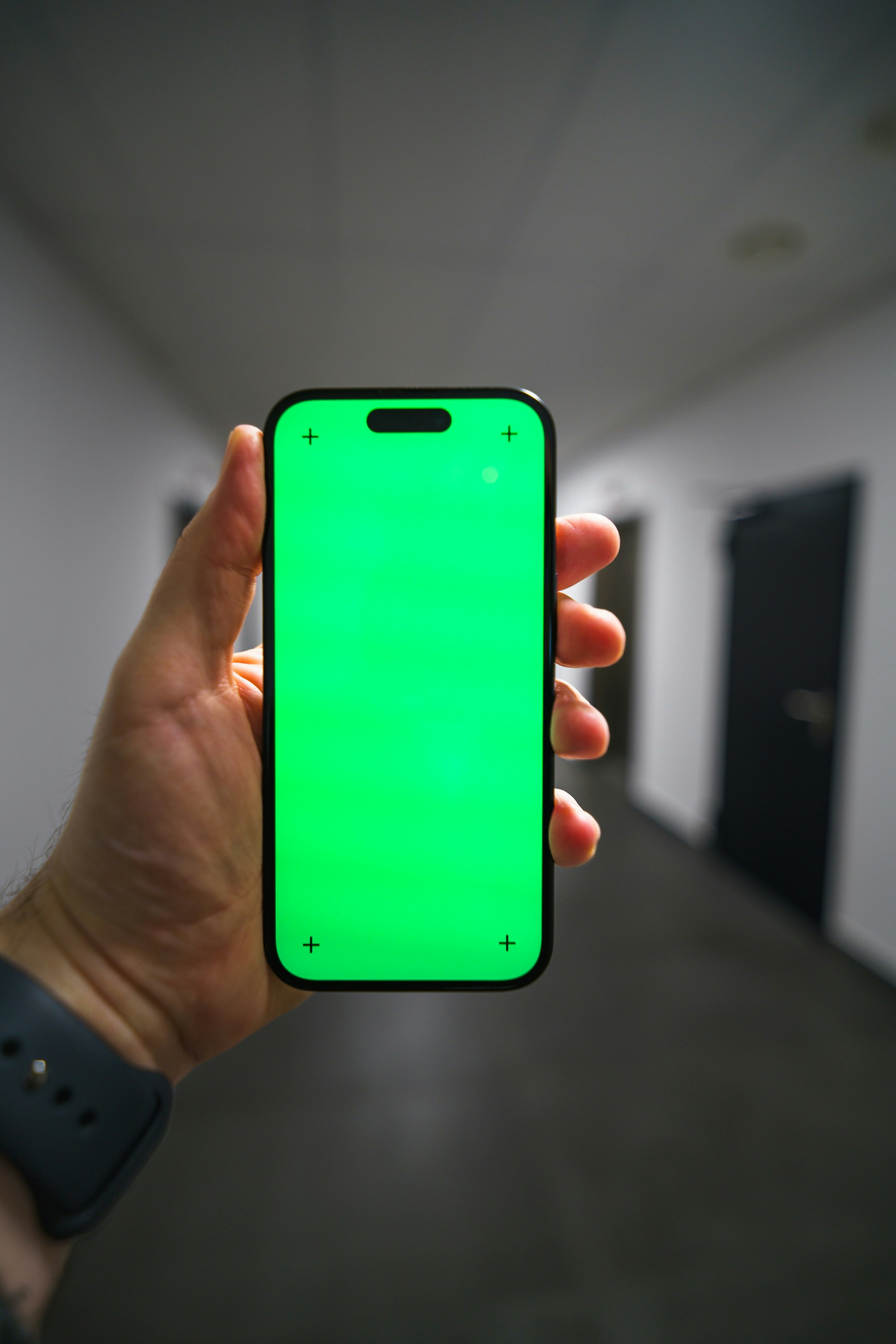 Hand holding a smartphone with a green screen.