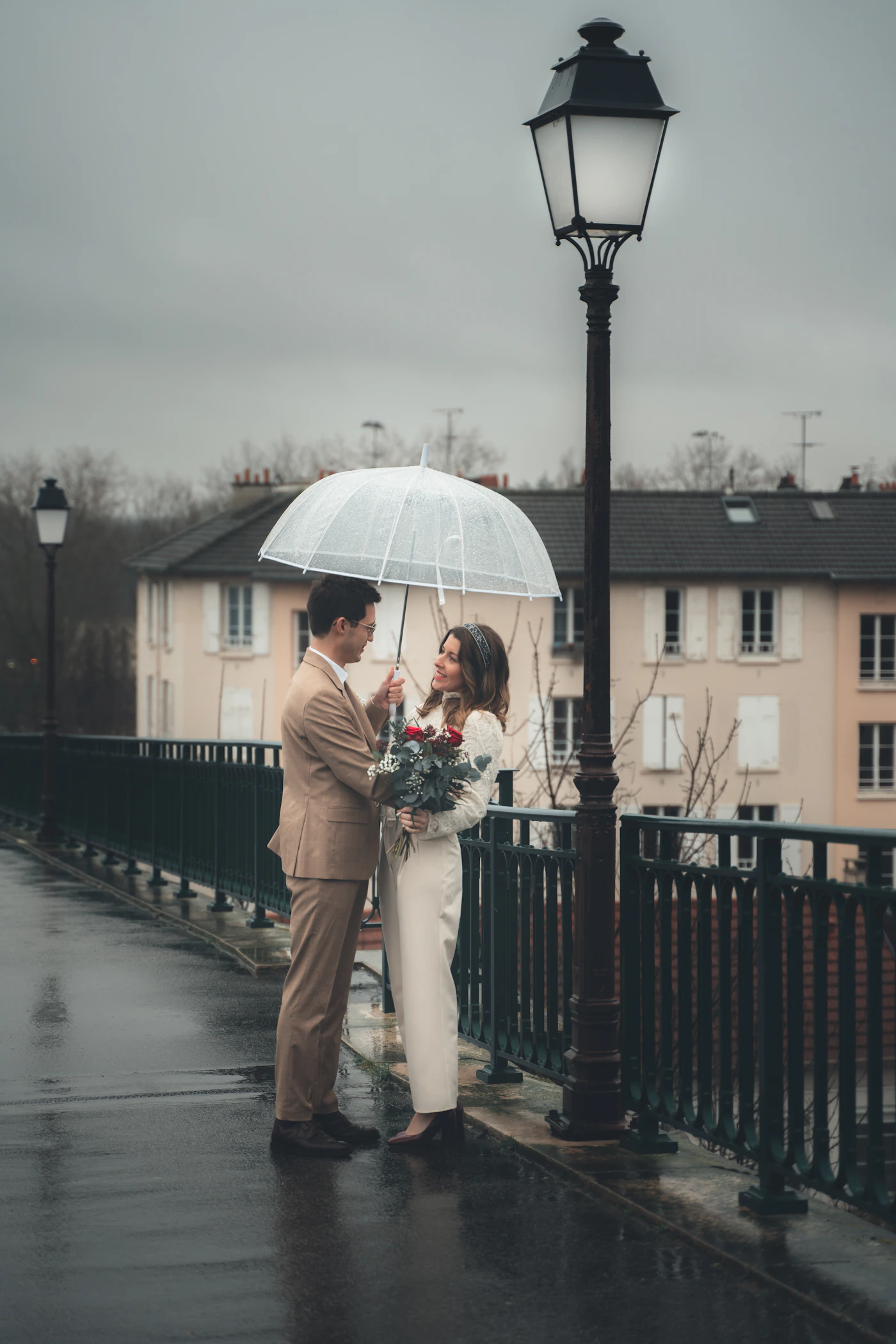 Couple embracing together beneath an umbrella on a bridge during a rainy day