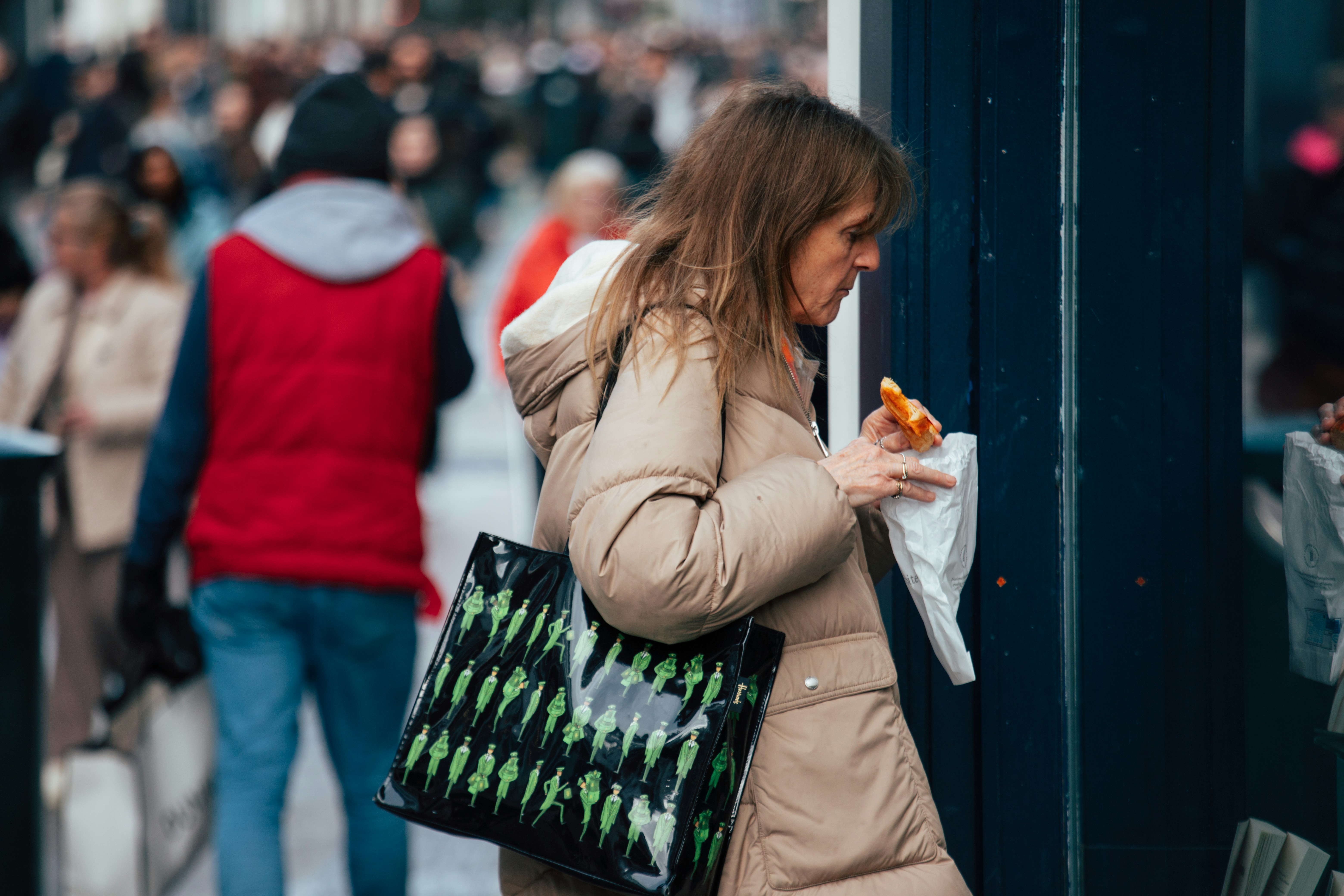 Woman in puffer jacket eating outdoors with shopping bag