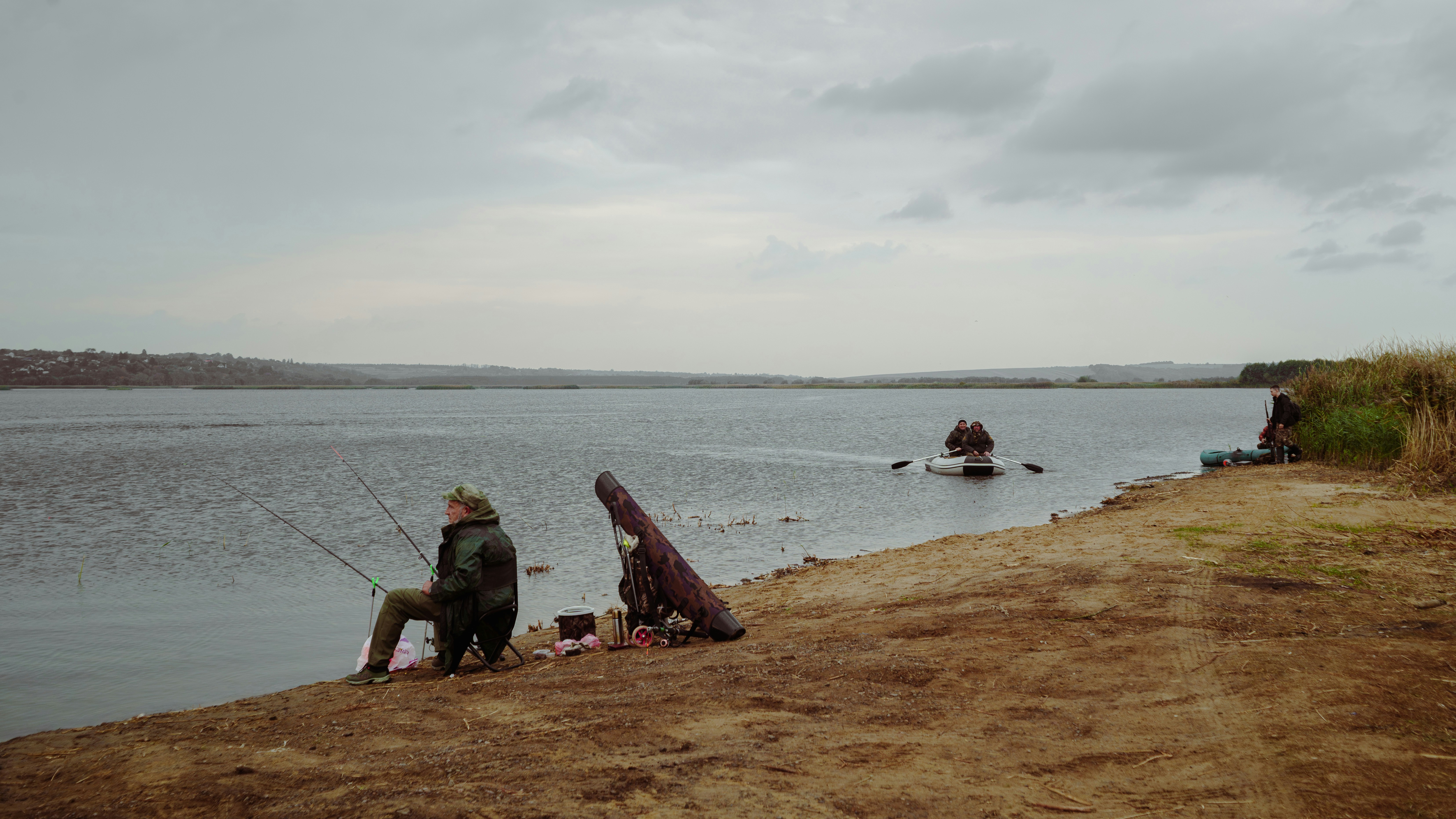 Two people fishing by a calm lake under cloudy sky