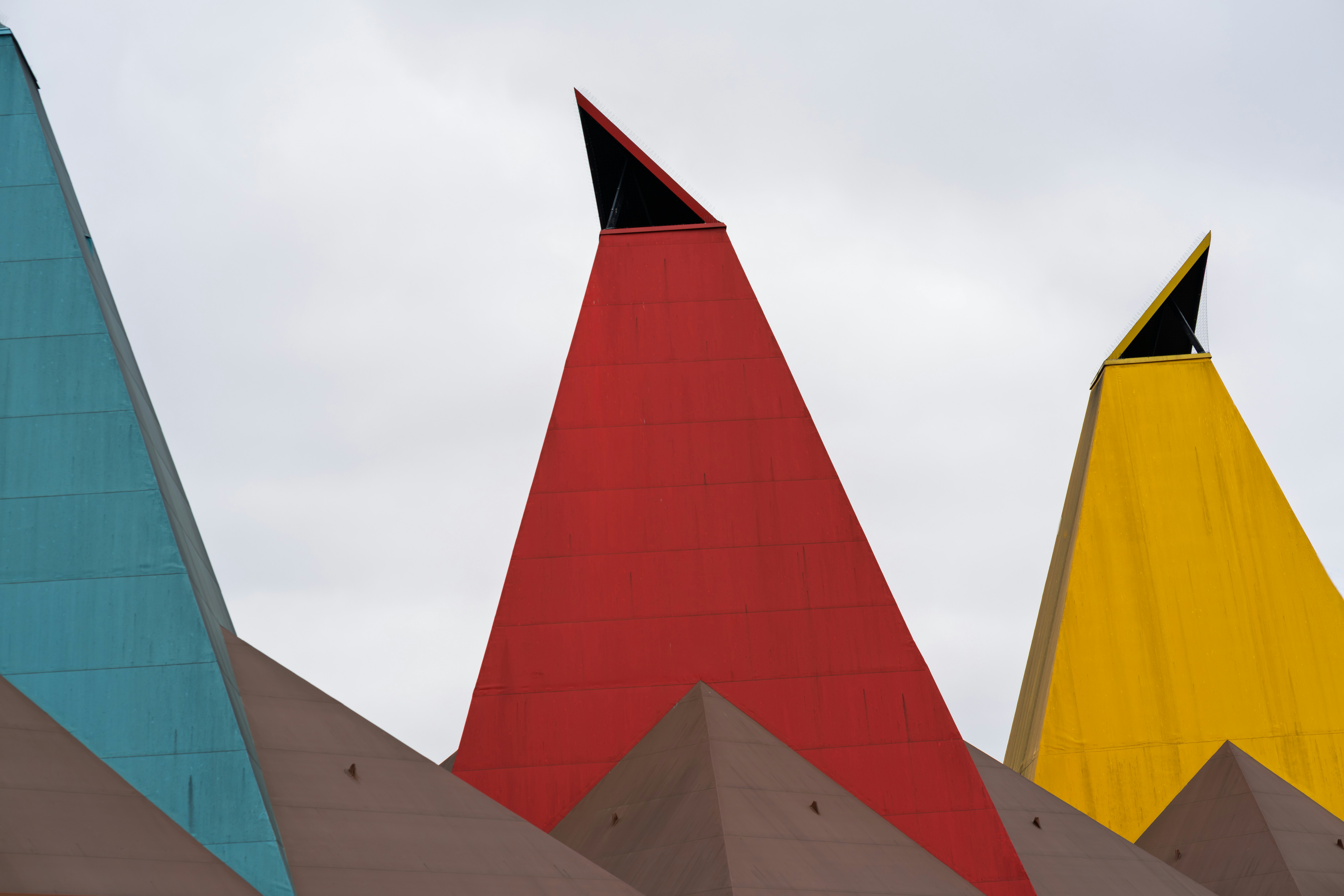 Three colorful geometric roof peaks against a cloudy sky