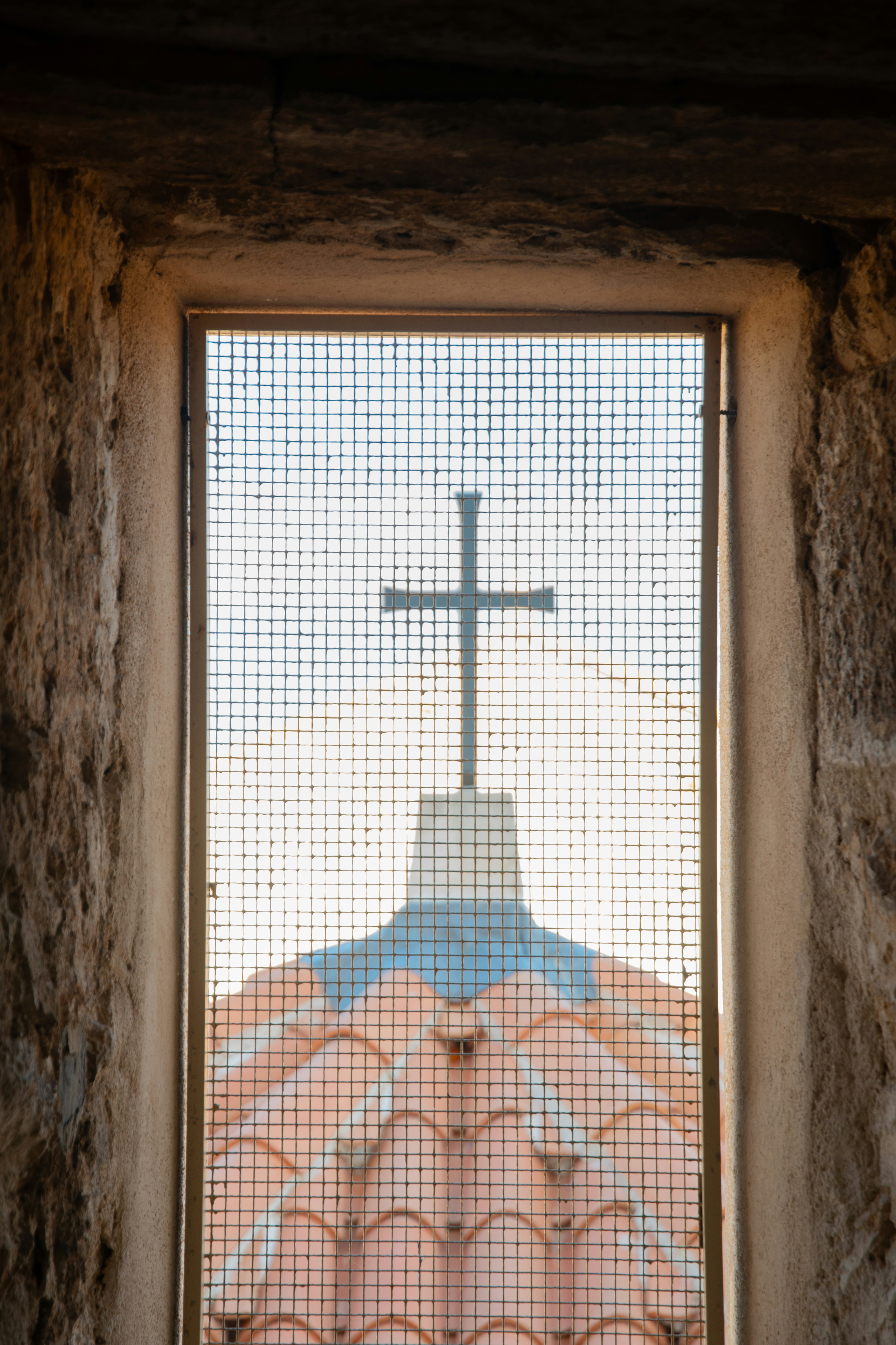 Croce sopra un edificio visto attraverso una finestra