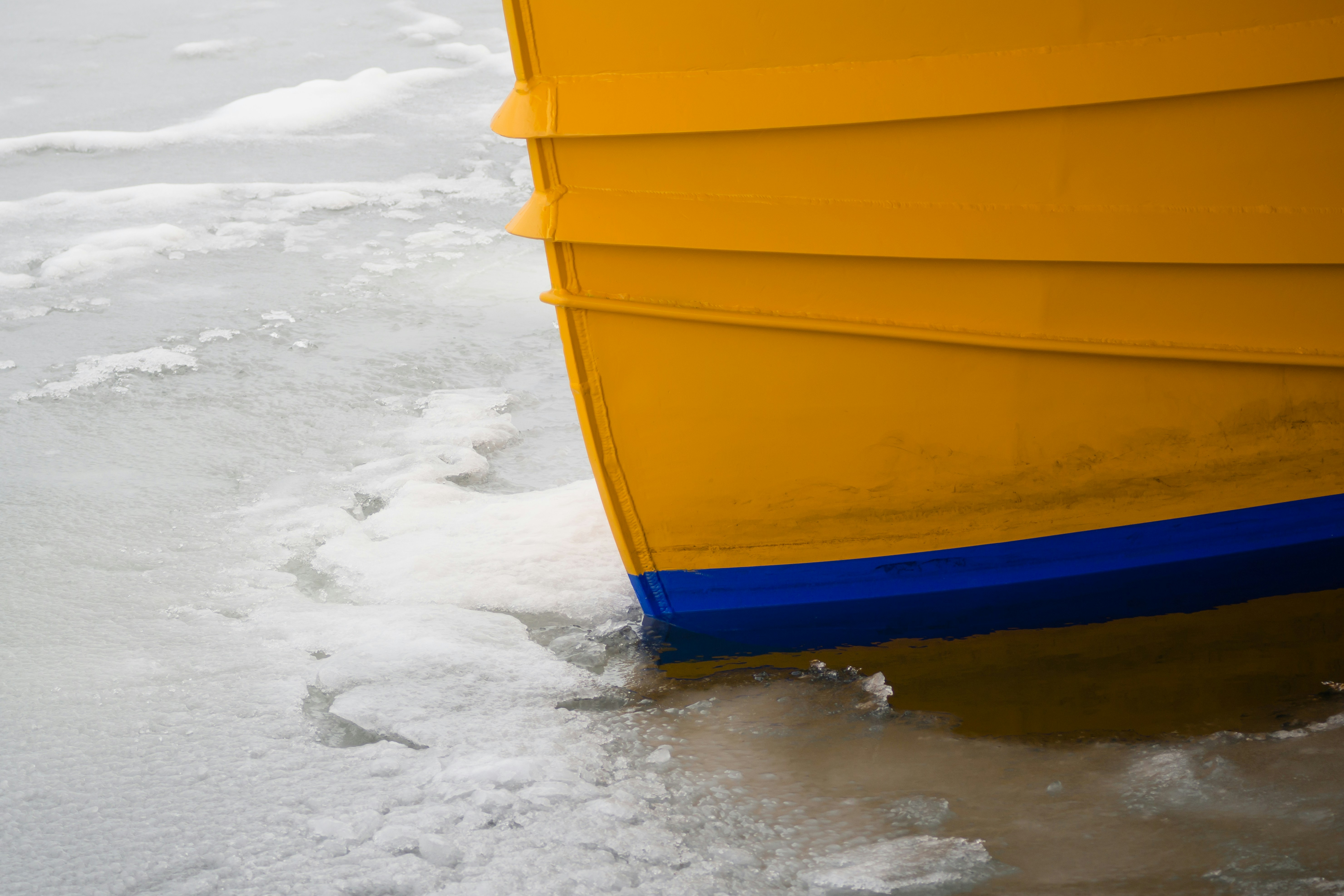 Ein gelber Bootsrumpf ruht auf eiskaltem Wasser.