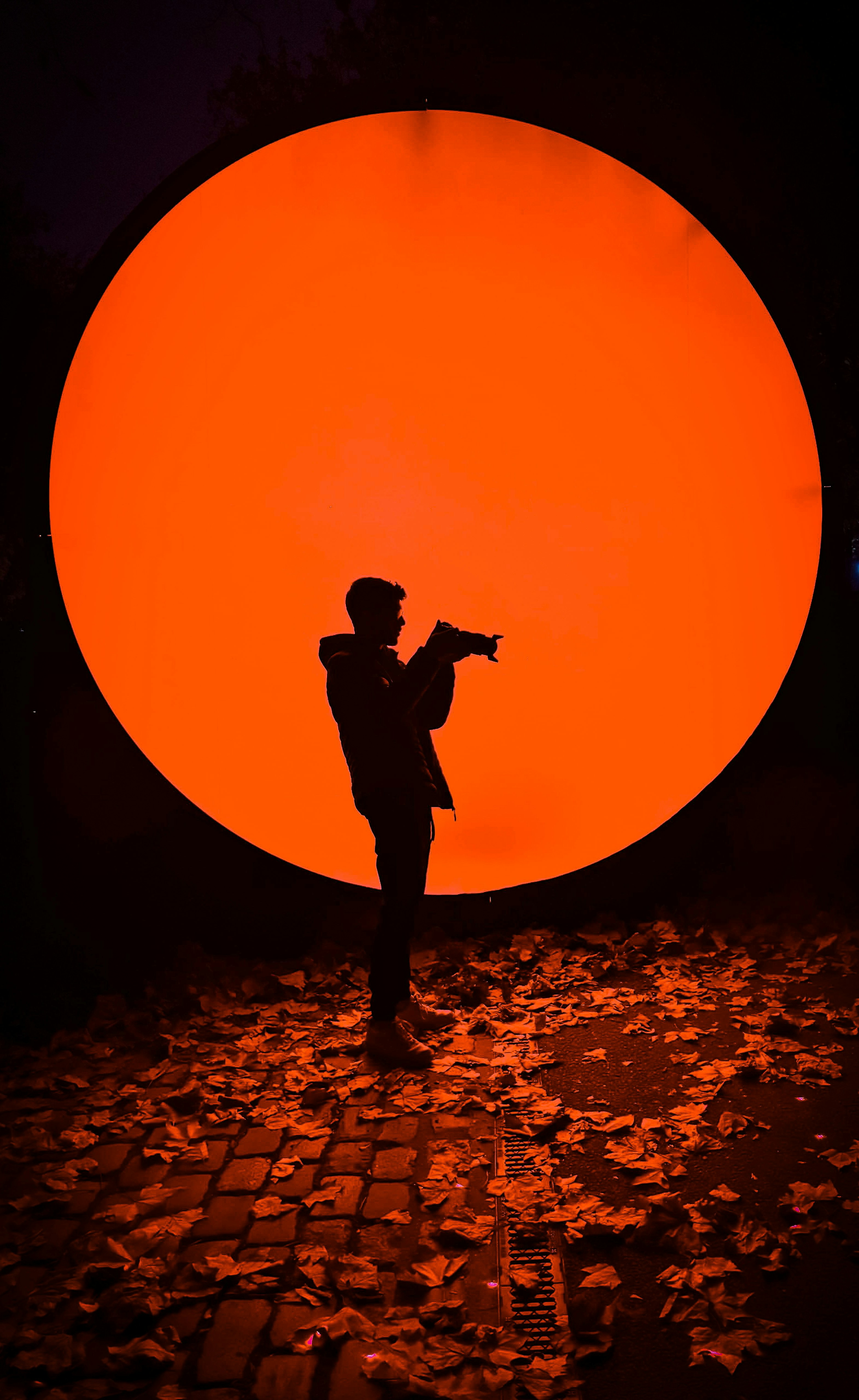 Silhouette of person holding camera against large orange circle