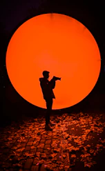 Silhouette of person holding camera against large orange circle