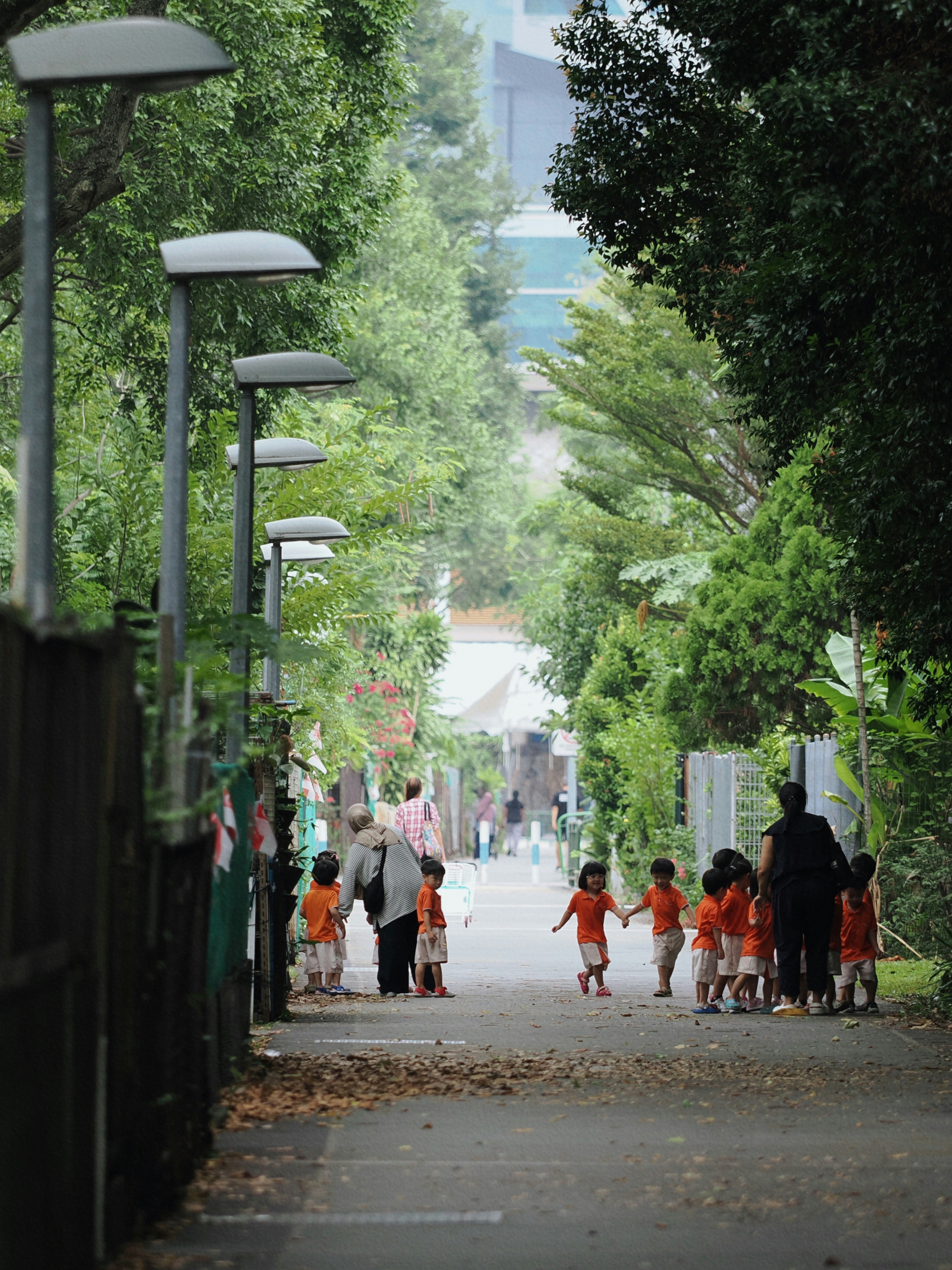 Kinder in orangefarbenen Hemden gehen mit Erwachsenen auf einem Weg.