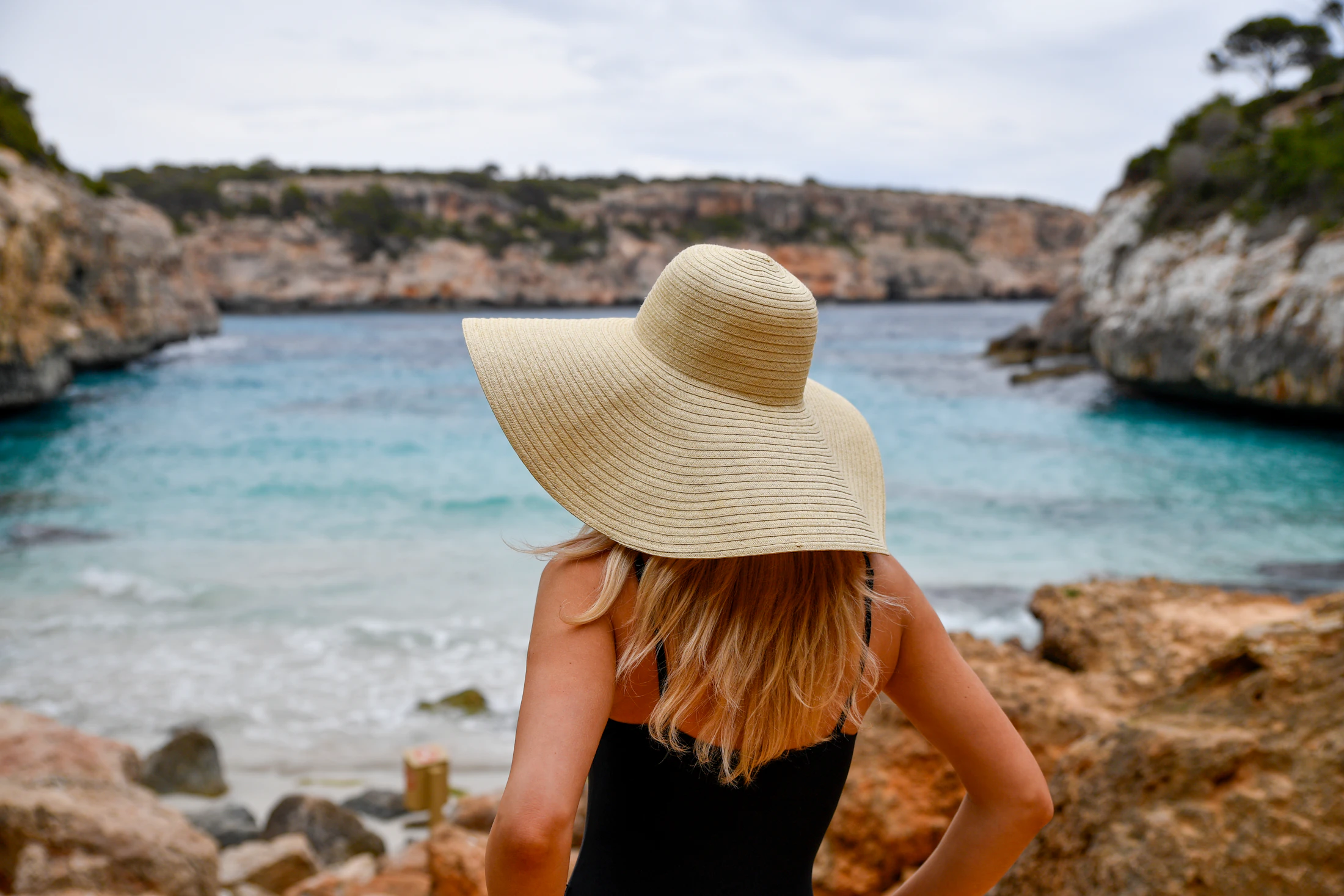 Femme au chapeau de paille face à une baie turquoise