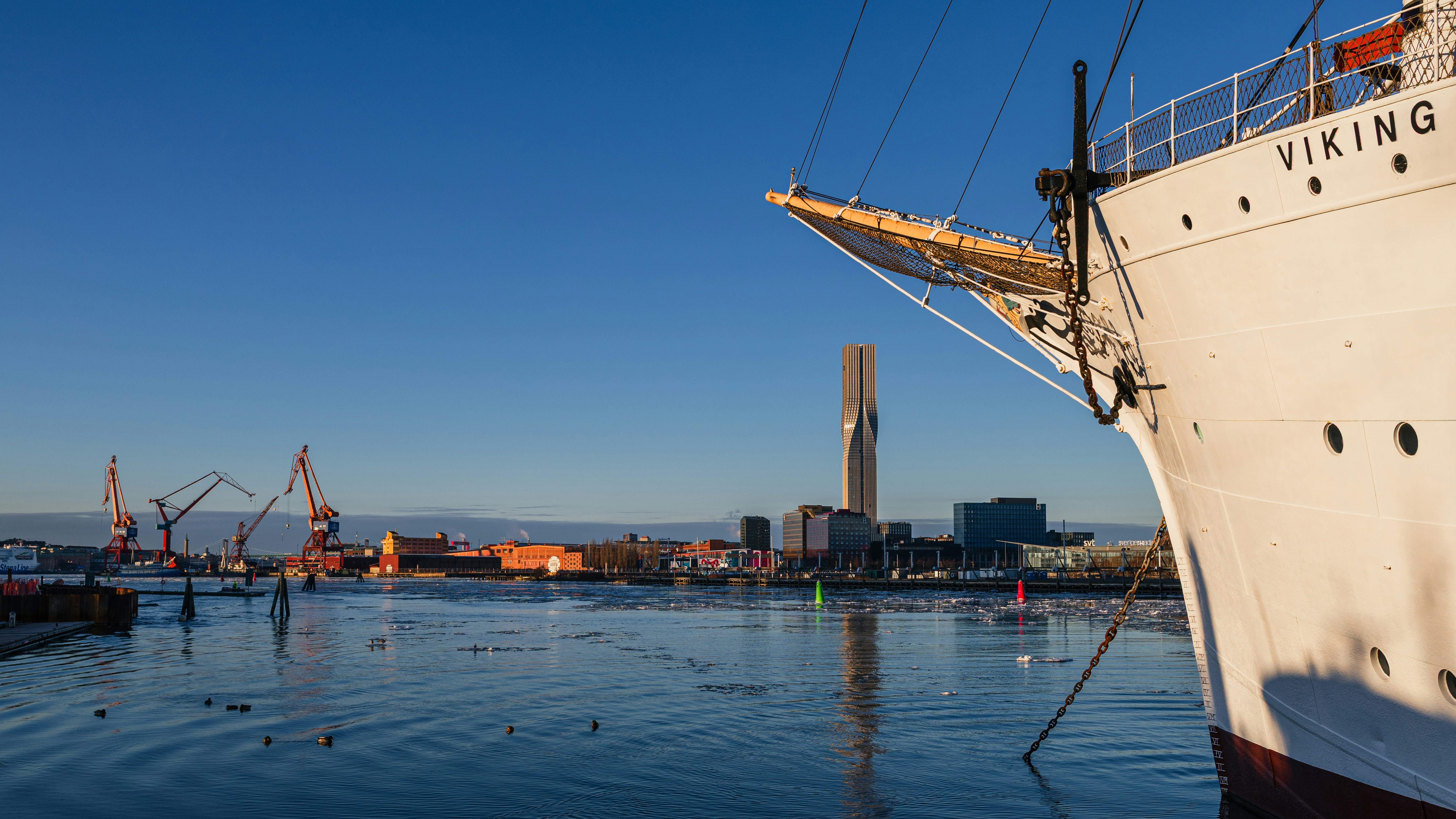 Large white ship docked in a harbor with city skyline.