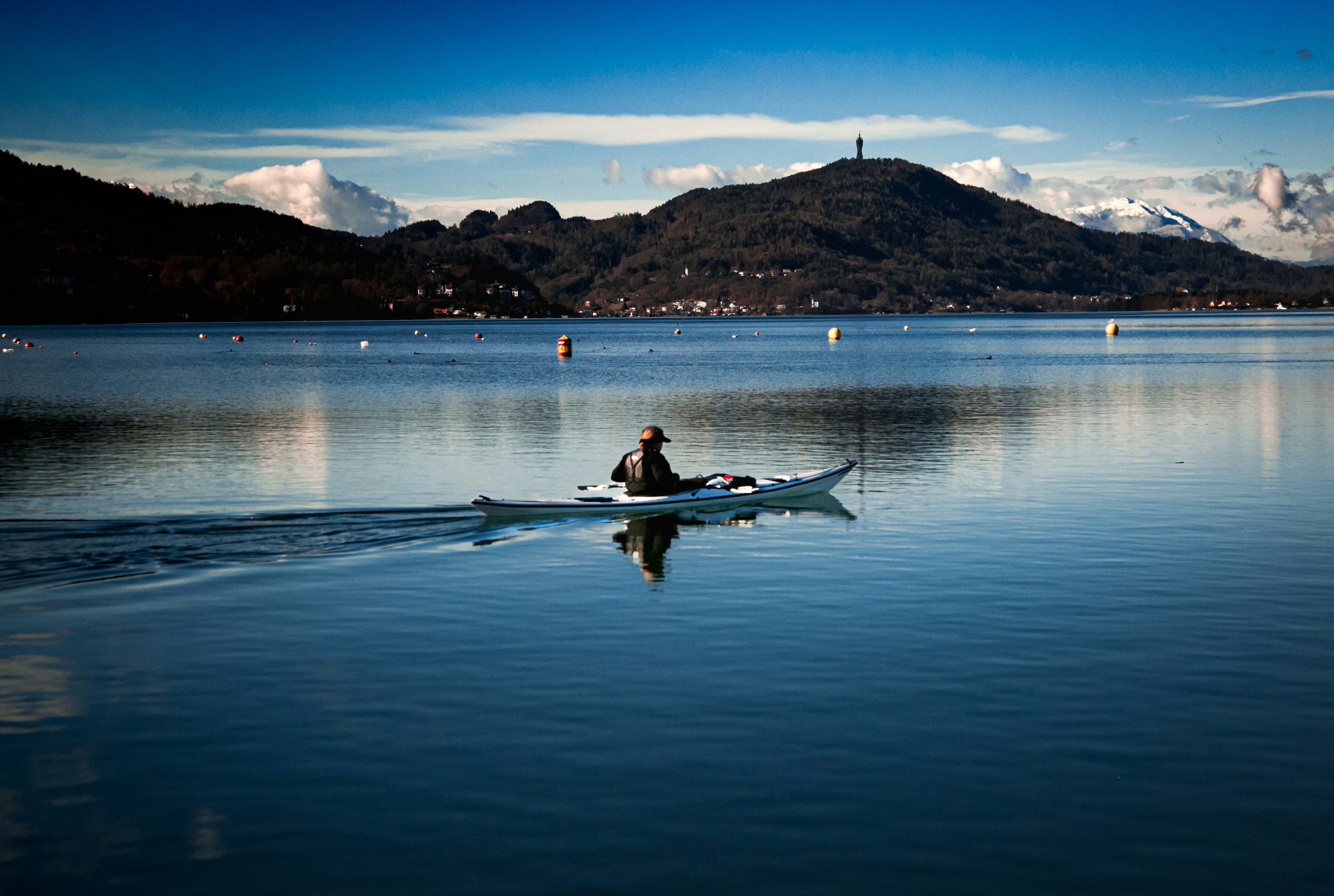 A person kayaks across a calm, reflective lake.