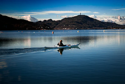 A person kayaks across a calm, reflective lake.