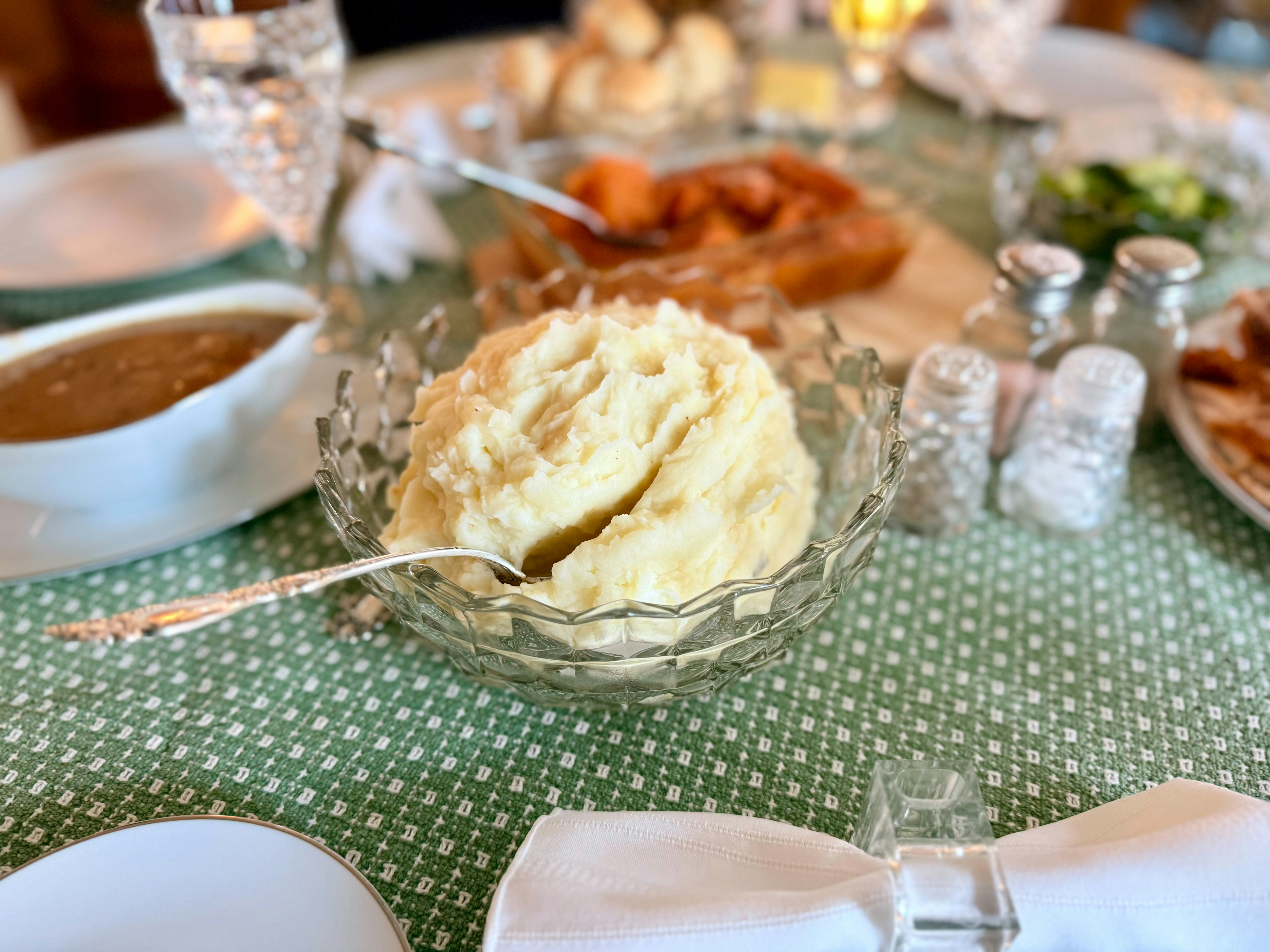 Mashed potatoes served in a crystal bowl on a table.