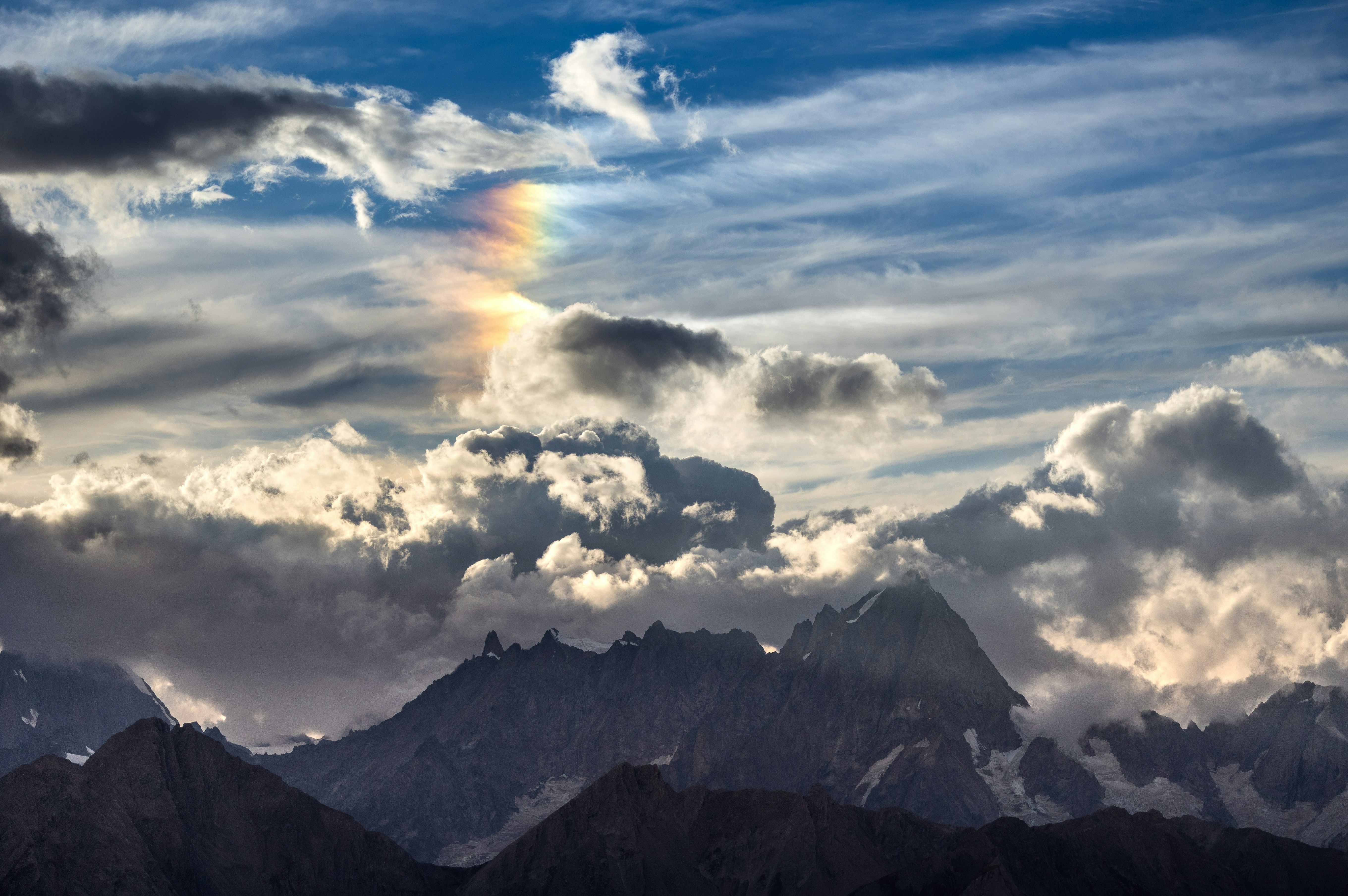 Rainbow arc in cloudy sky over jagged mountains