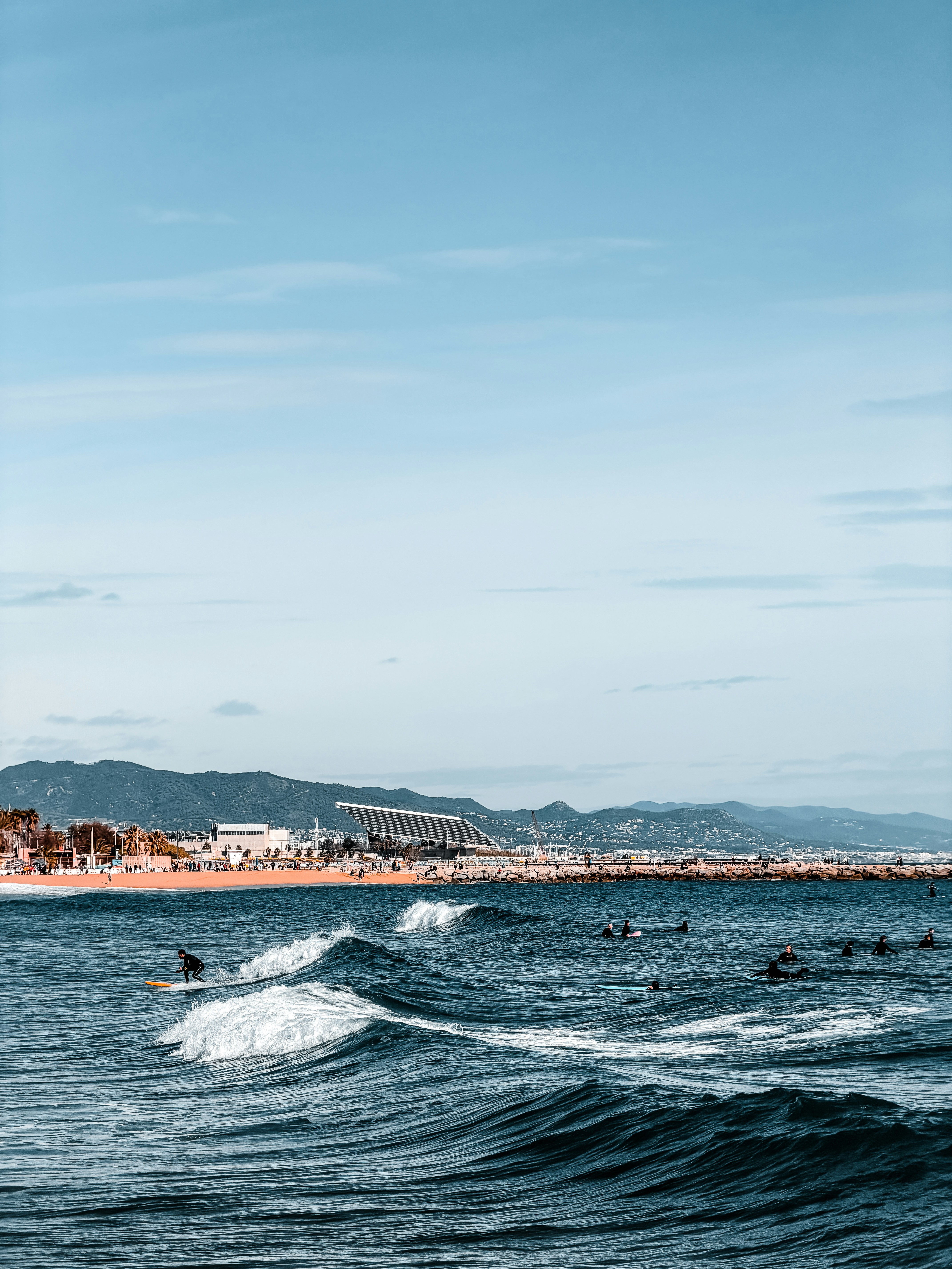 해안 도시 스카이라인 근처에서 파도를 타는 서퍼들