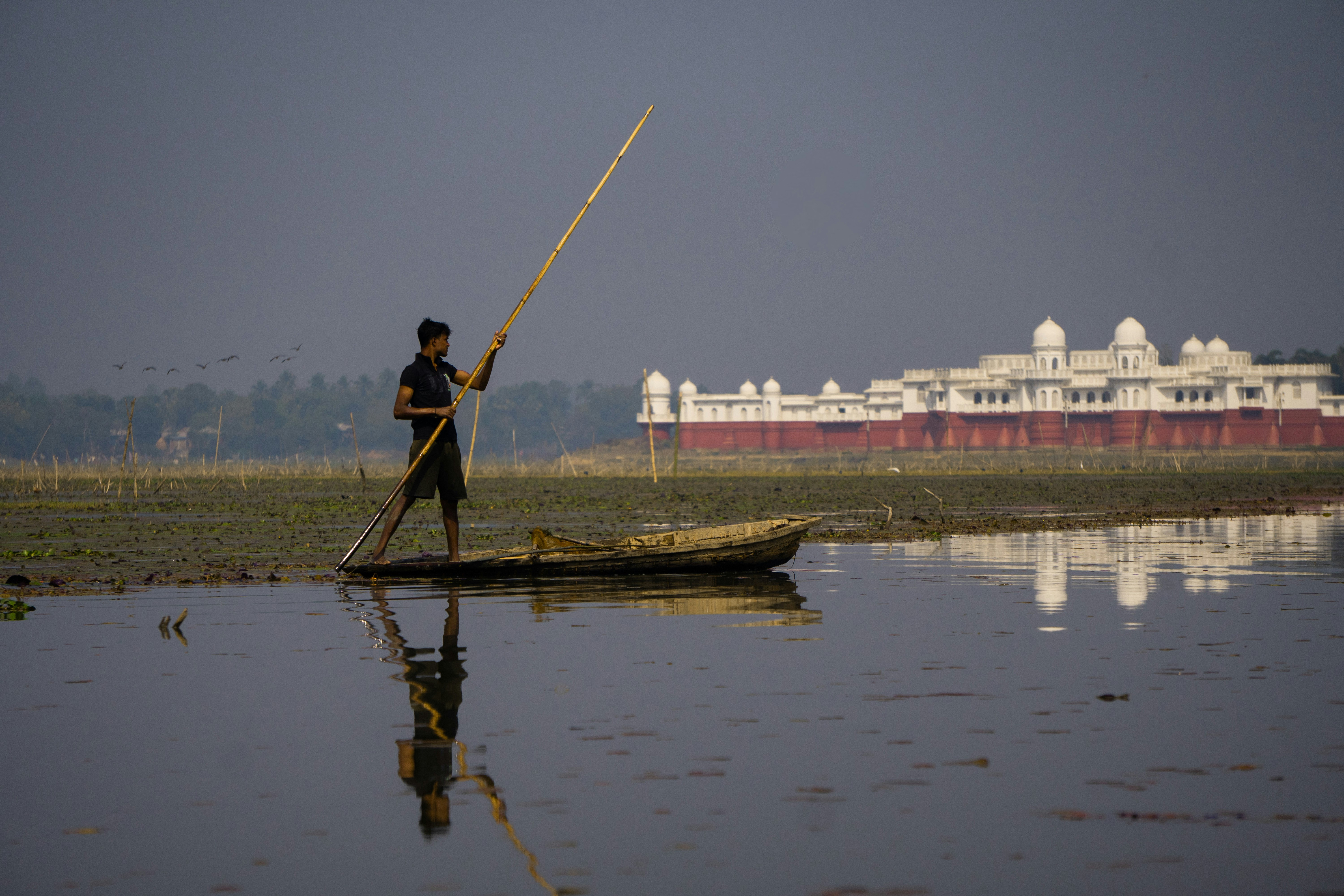 Man poles boat on water with building in background