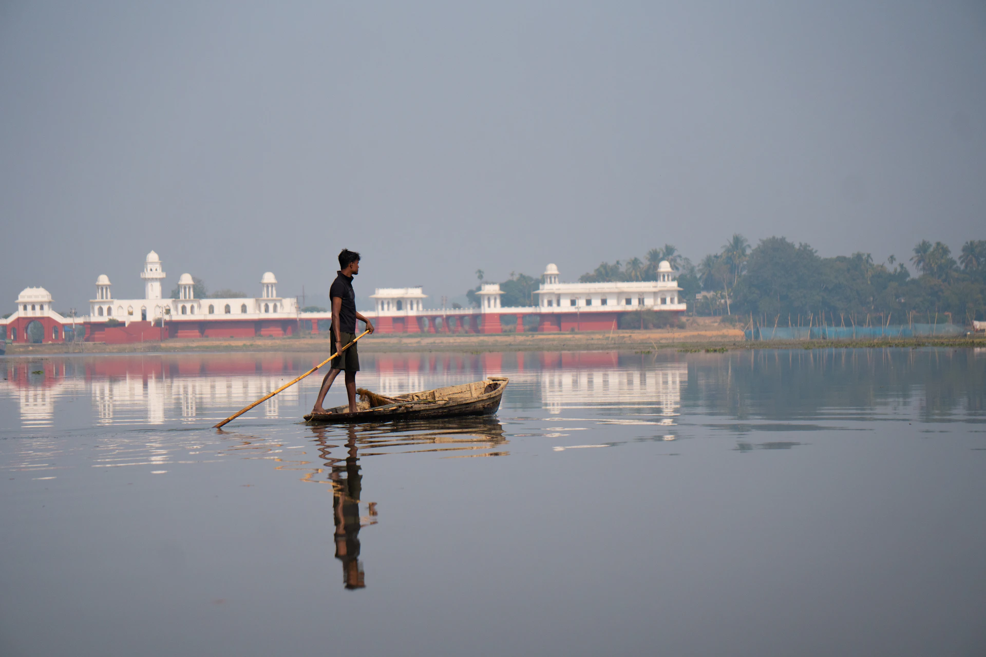 Man rows boat on calm water with white building