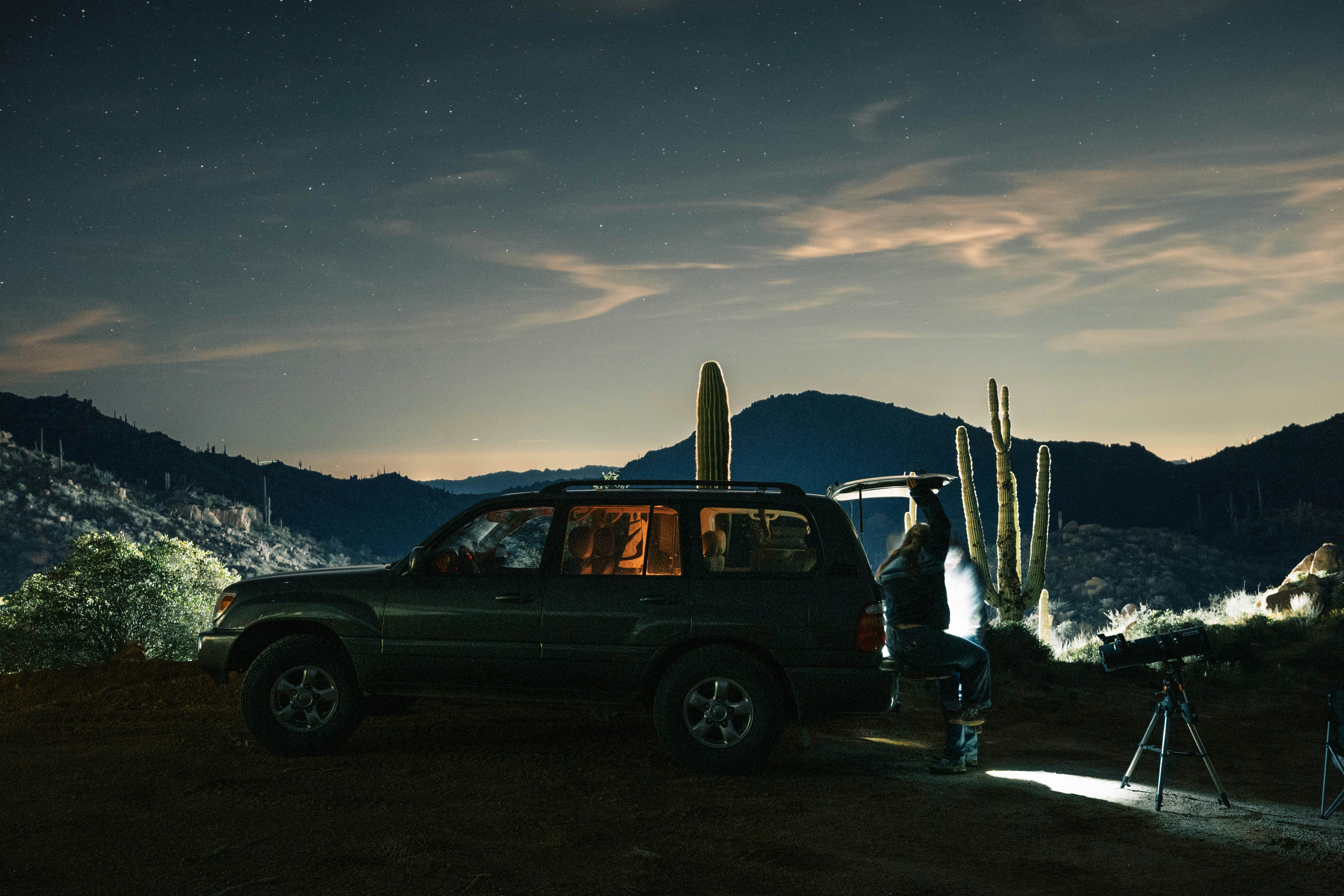 Mann, der nachts mit dem Teleskop neben dem SUV Sterne beobachtet