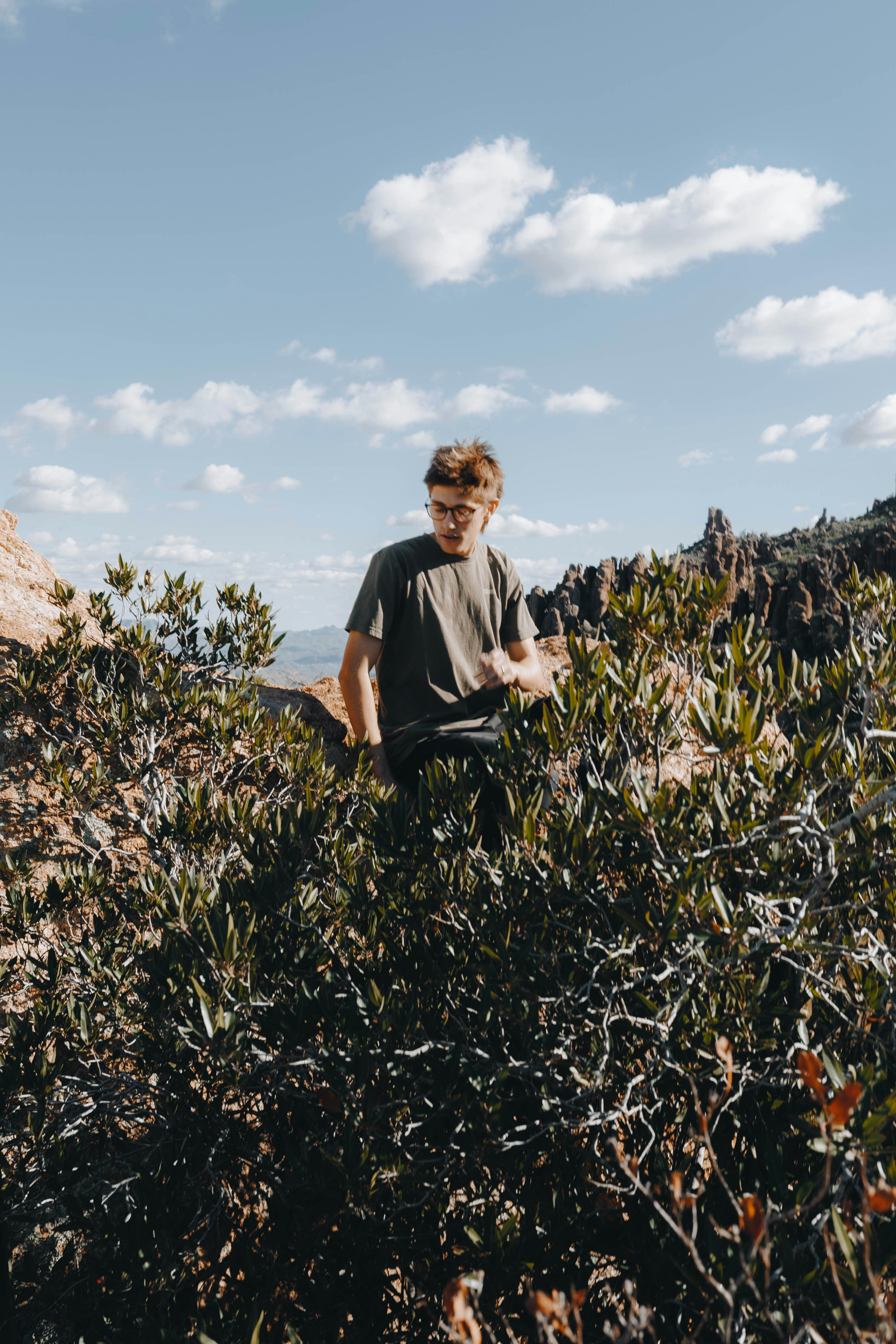 Junger Mann, der auf einem felsigen, strauchbedeckten Hügel steht.