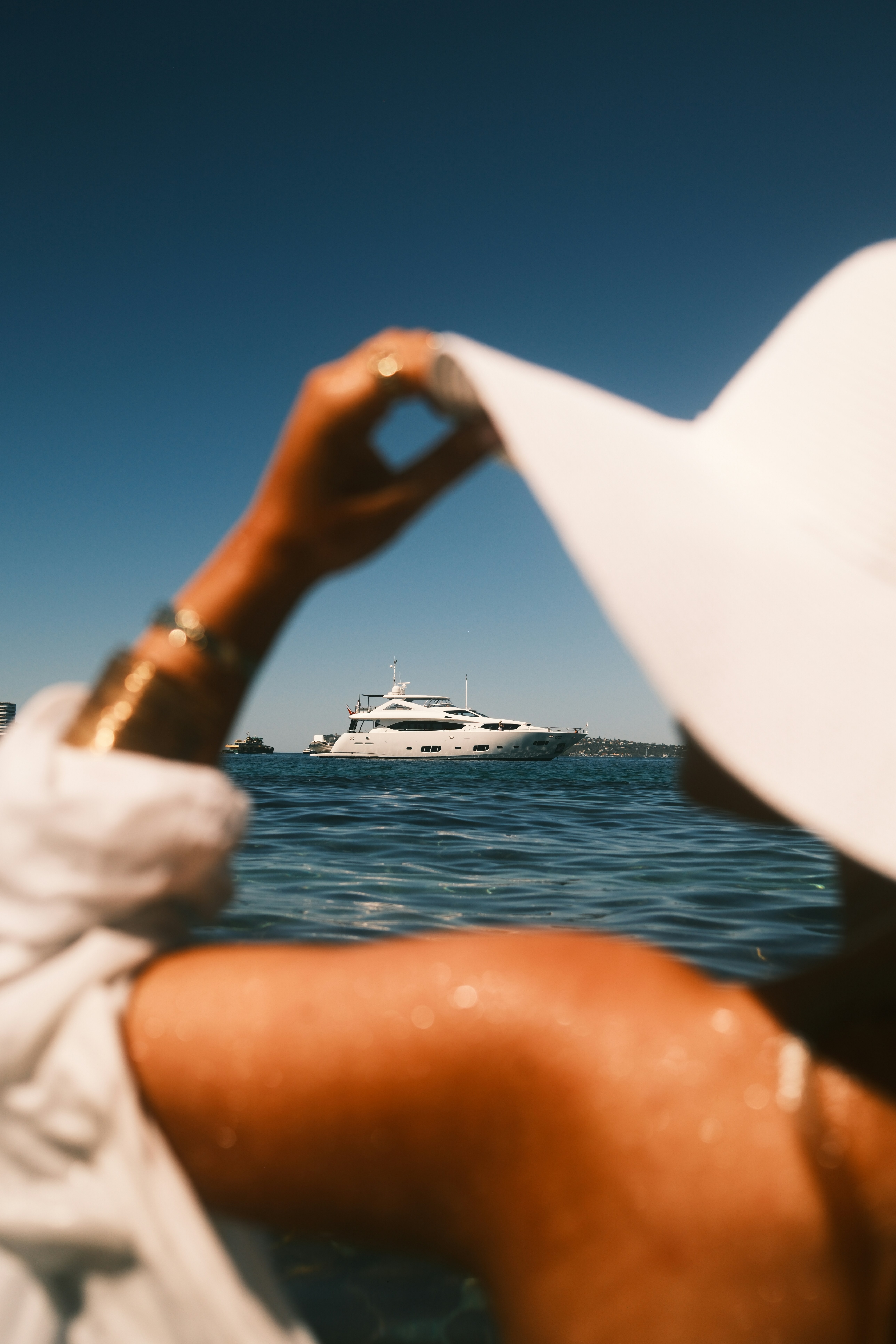 Woman in white hat looks at yacht on the water