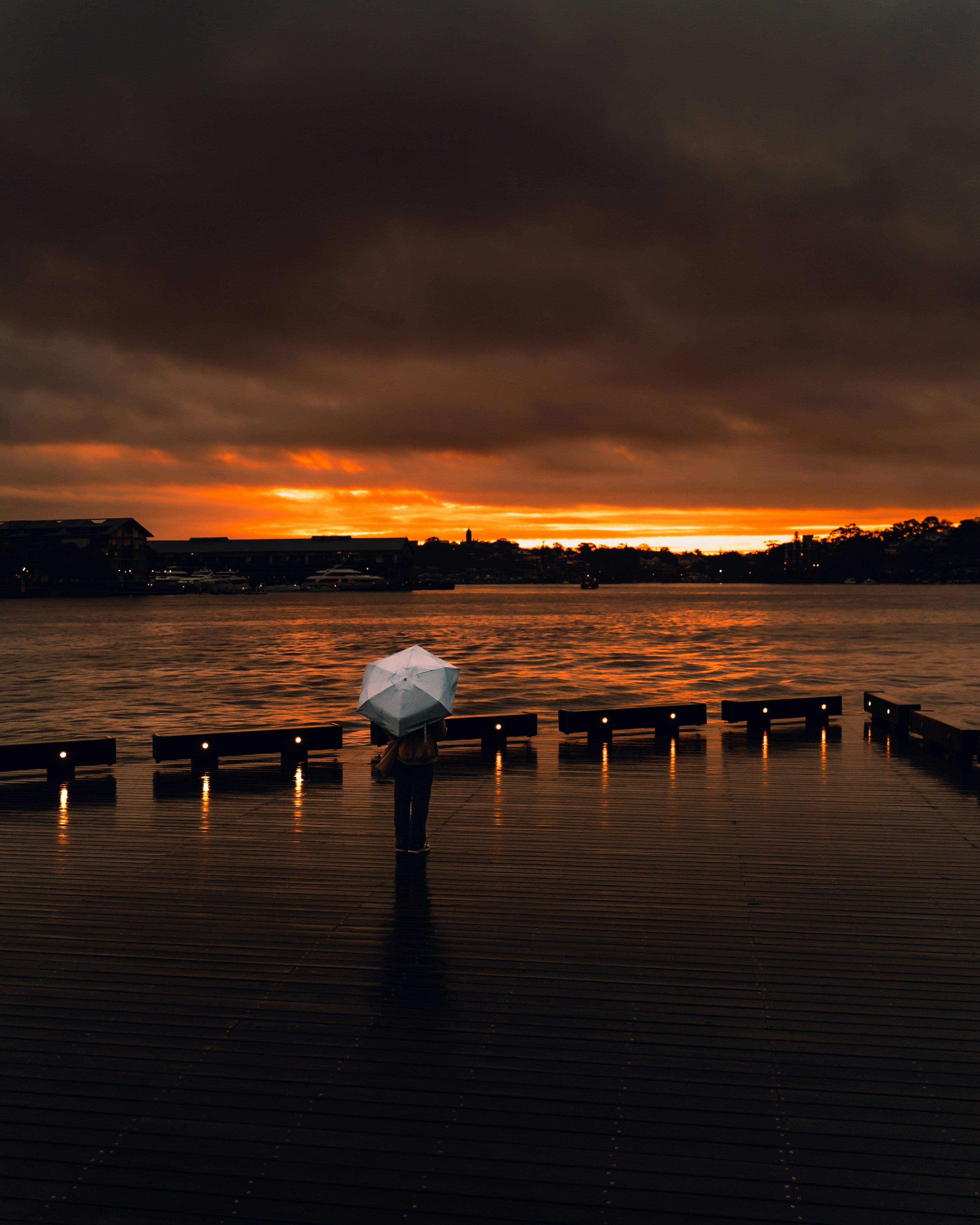 Person with umbrella on wet pier at sunset