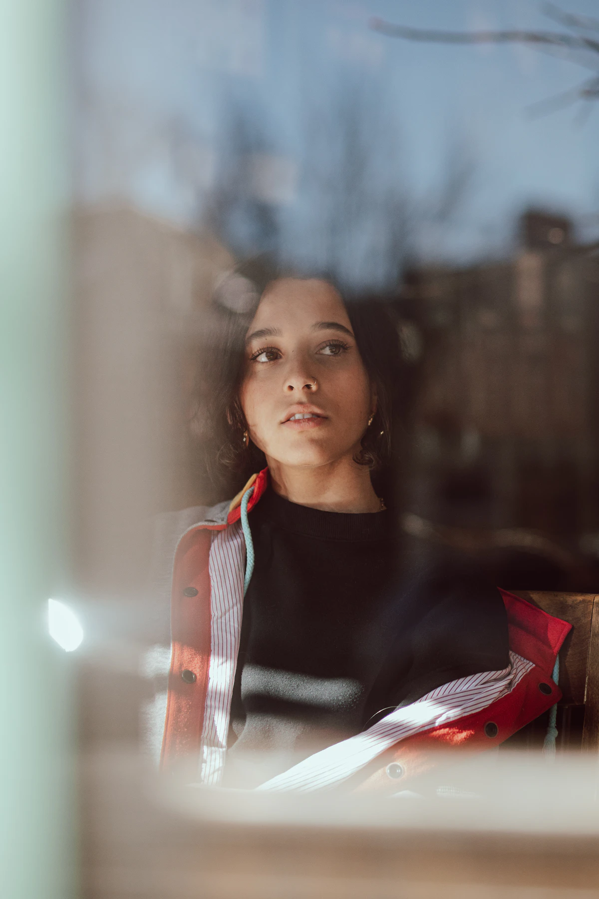 Young woman gazing through a window, reflections layered over her face — second-generation identity therapy Ontario