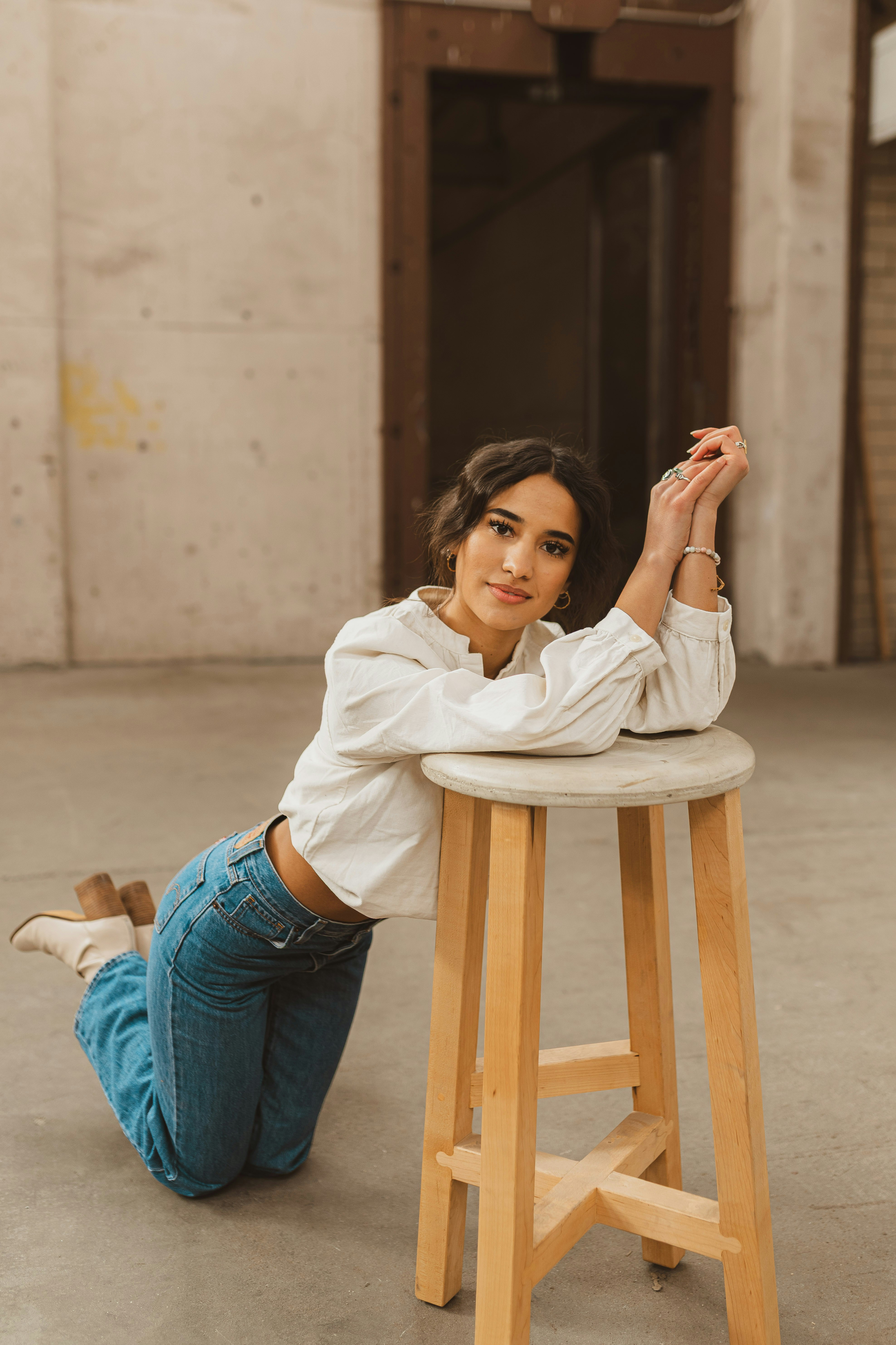 A young woman in jeans leans on a stool