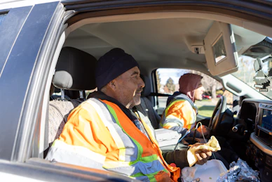 Two men in reflective vests eating in a truck.