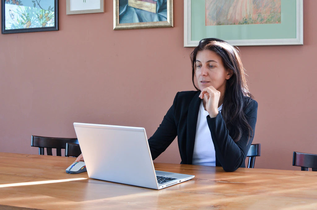 Woman in a black blazer working on a laptop.