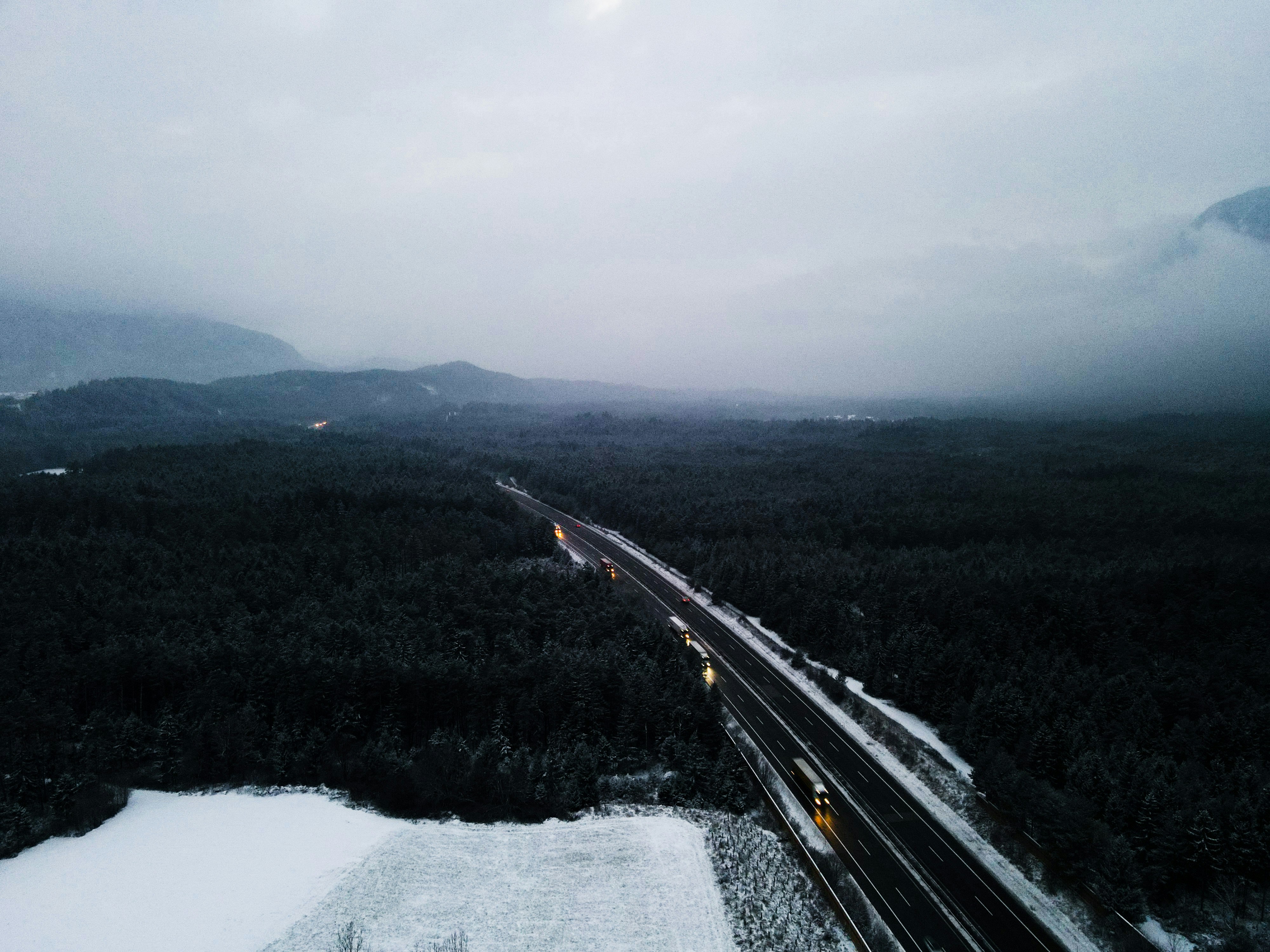Snowy highway through dark forest with mountains.