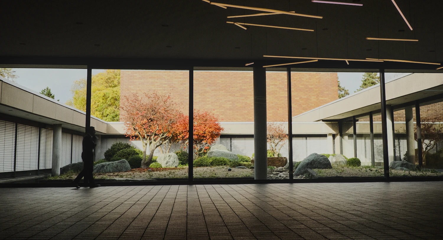 A long glazed walkway running past a planted courtyard at dusk
