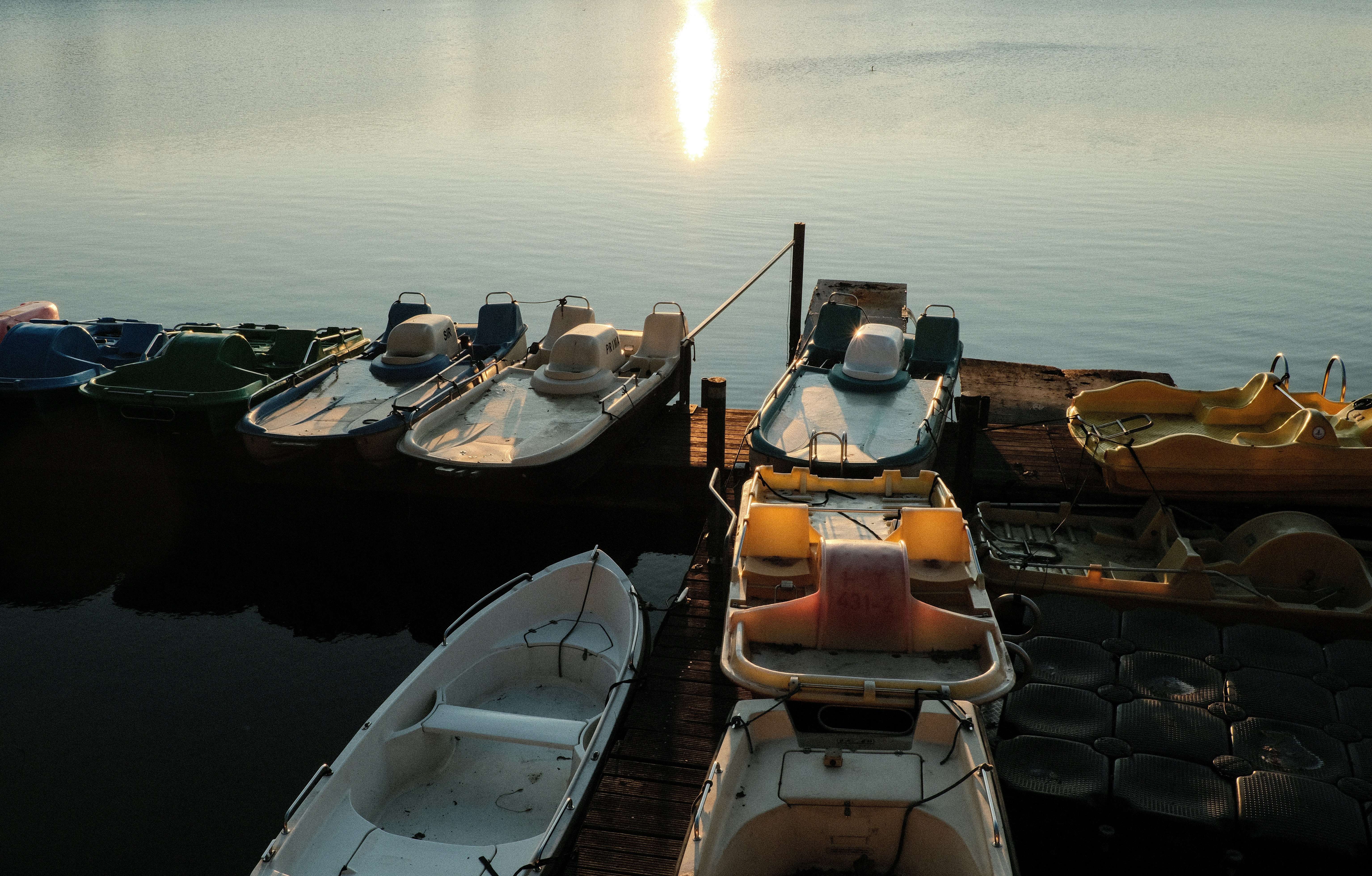 Several paddle boats docked on a wooden pier at sunset.