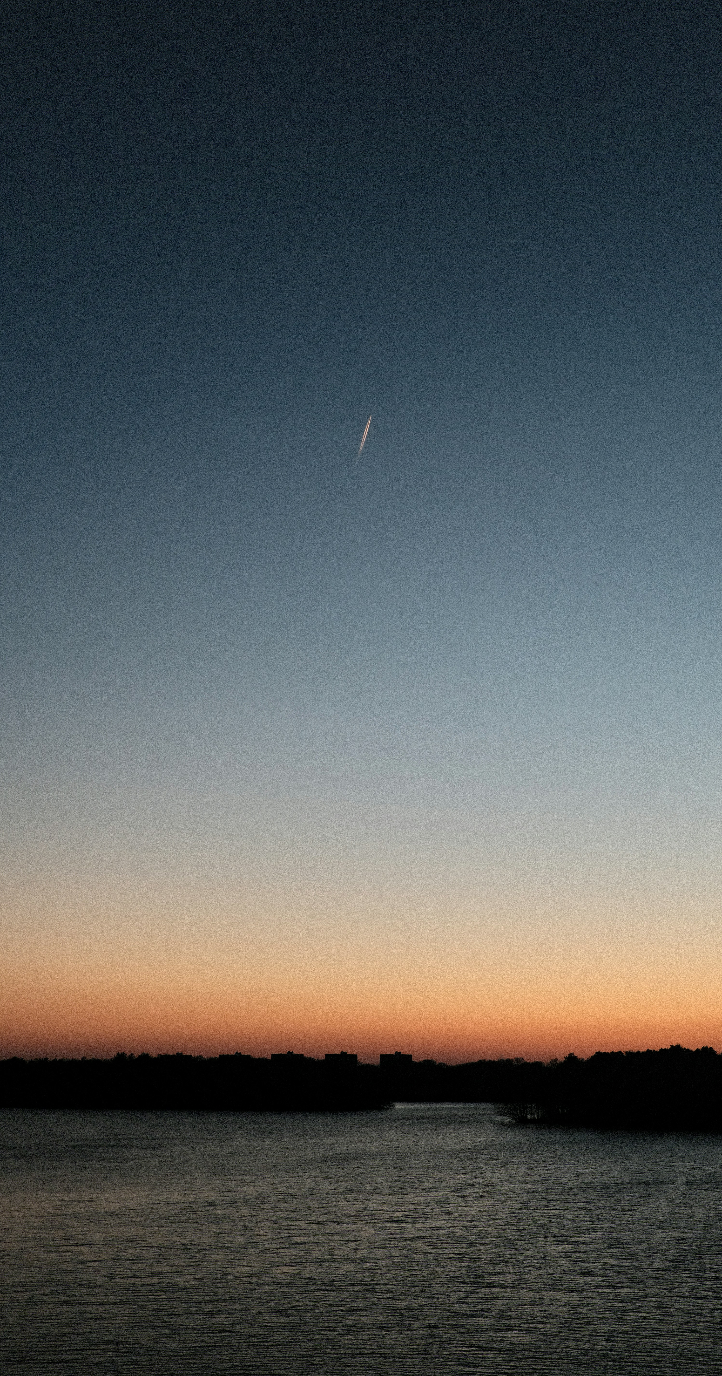 Airplane contrail in the sky over a dark horizon.