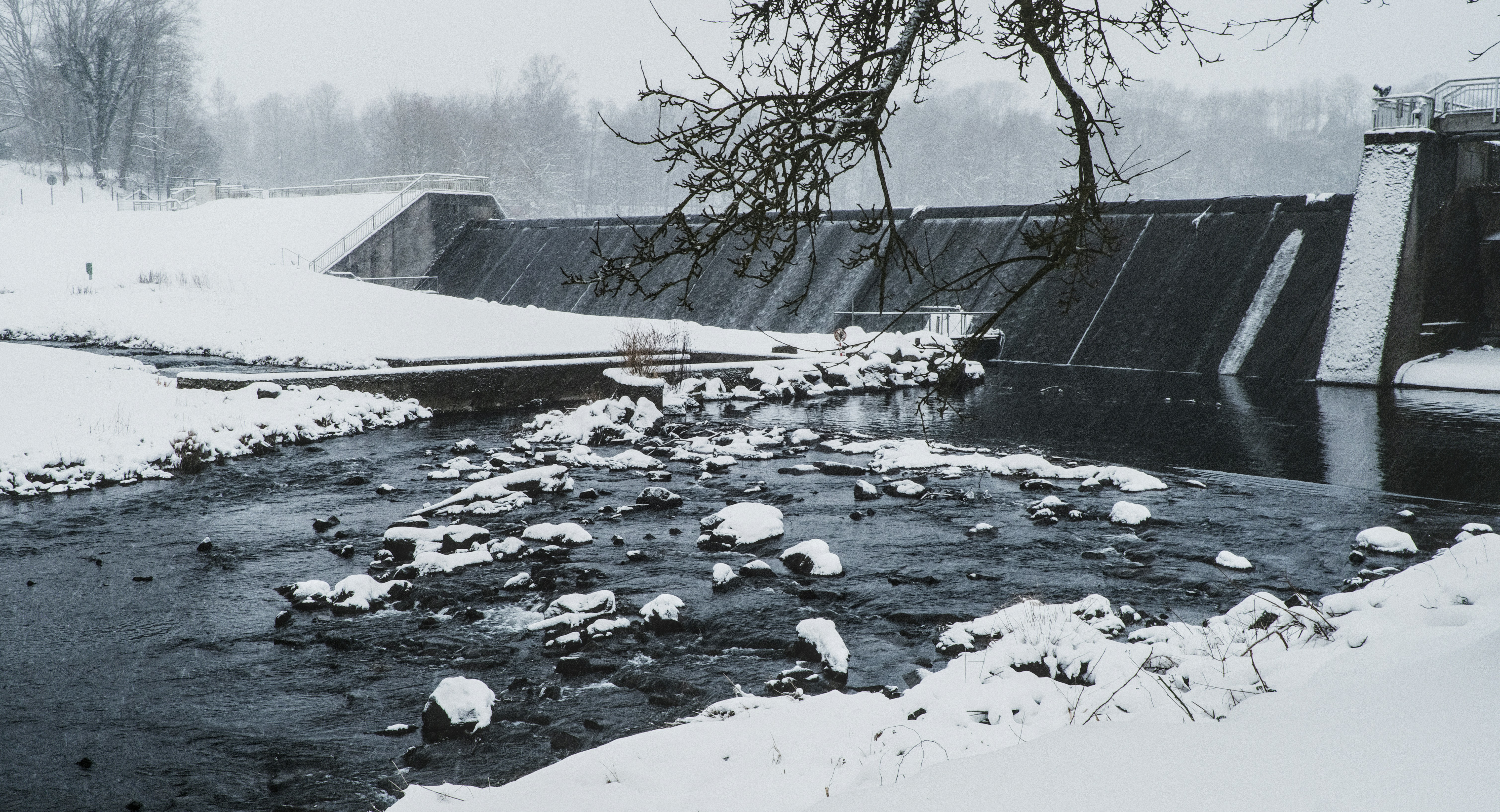Snowy dam with a flowing river and bare trees