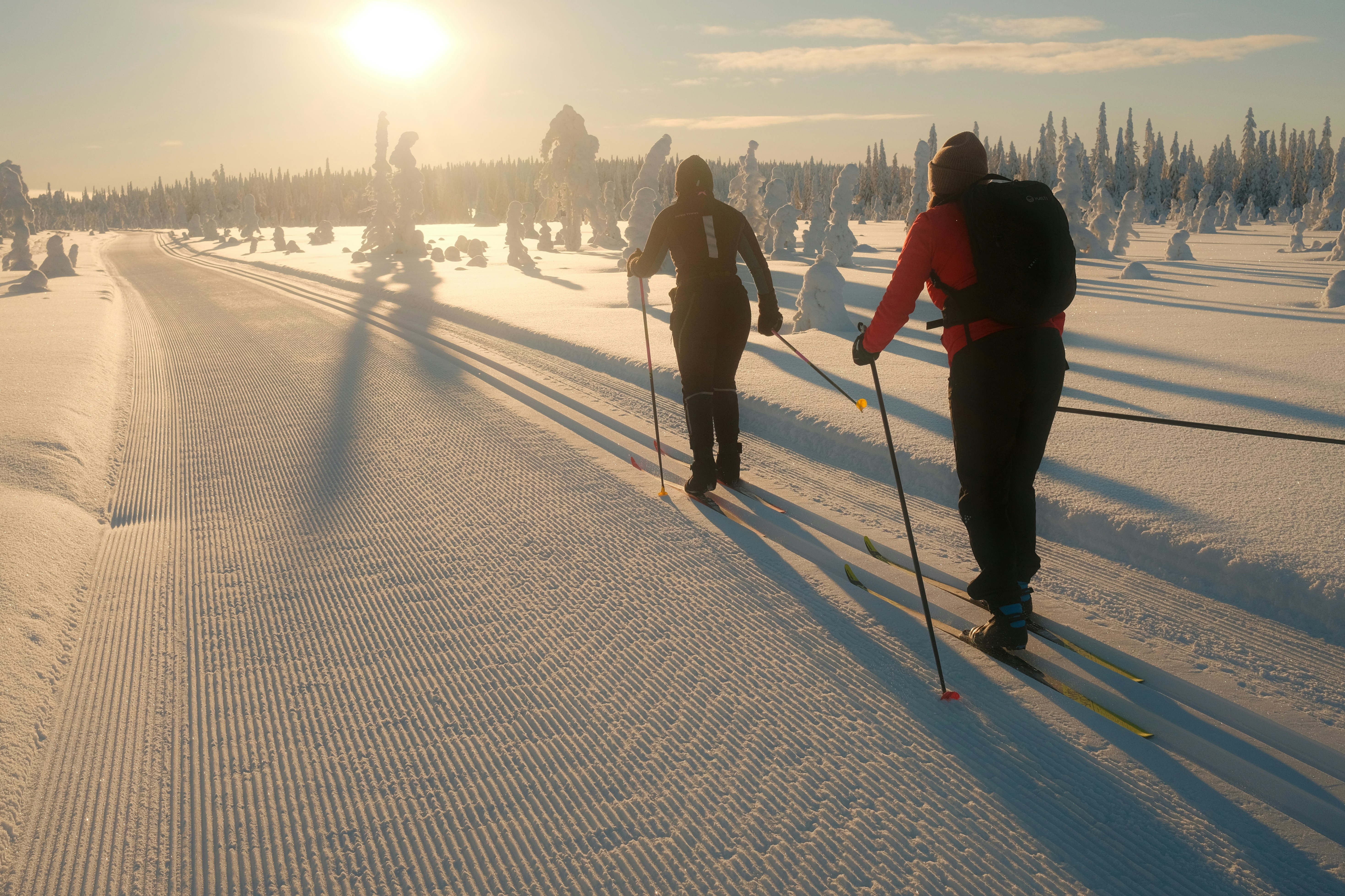Two people cross-country skiing on a snowy path at sunset.