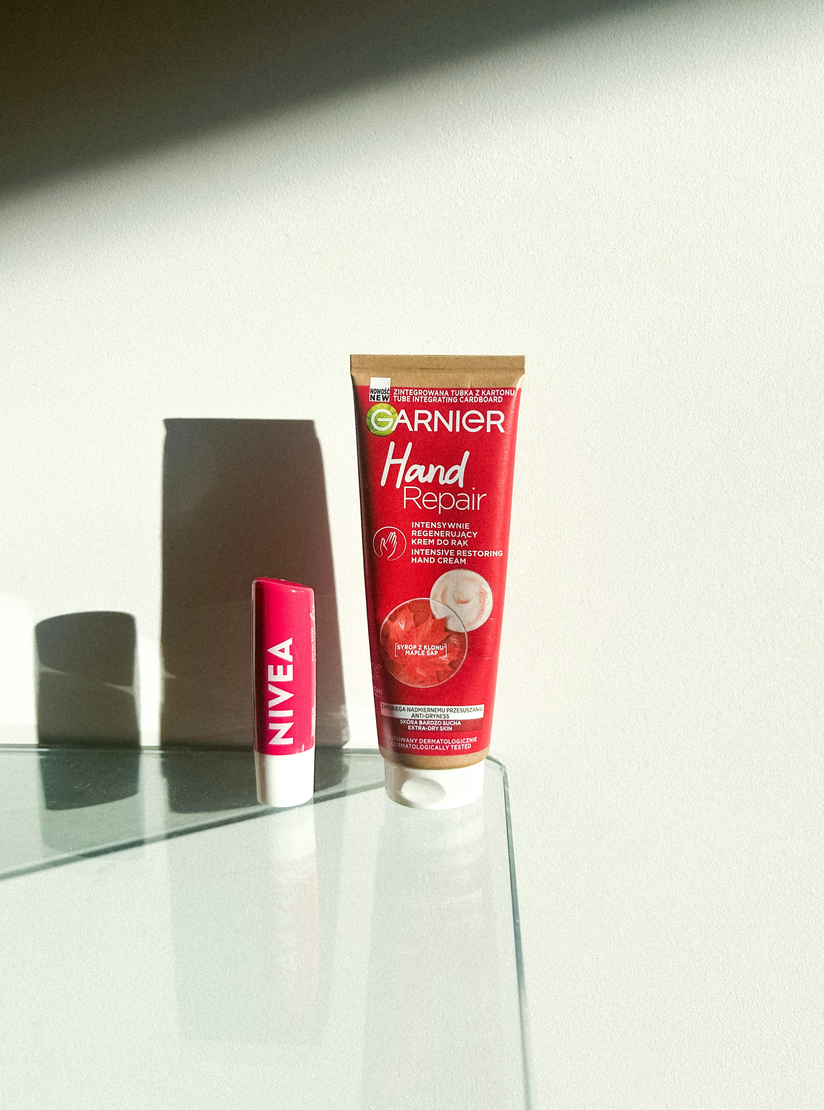 Crème pour les mains Garnier et baume à lèvres Nivea sur table en verre