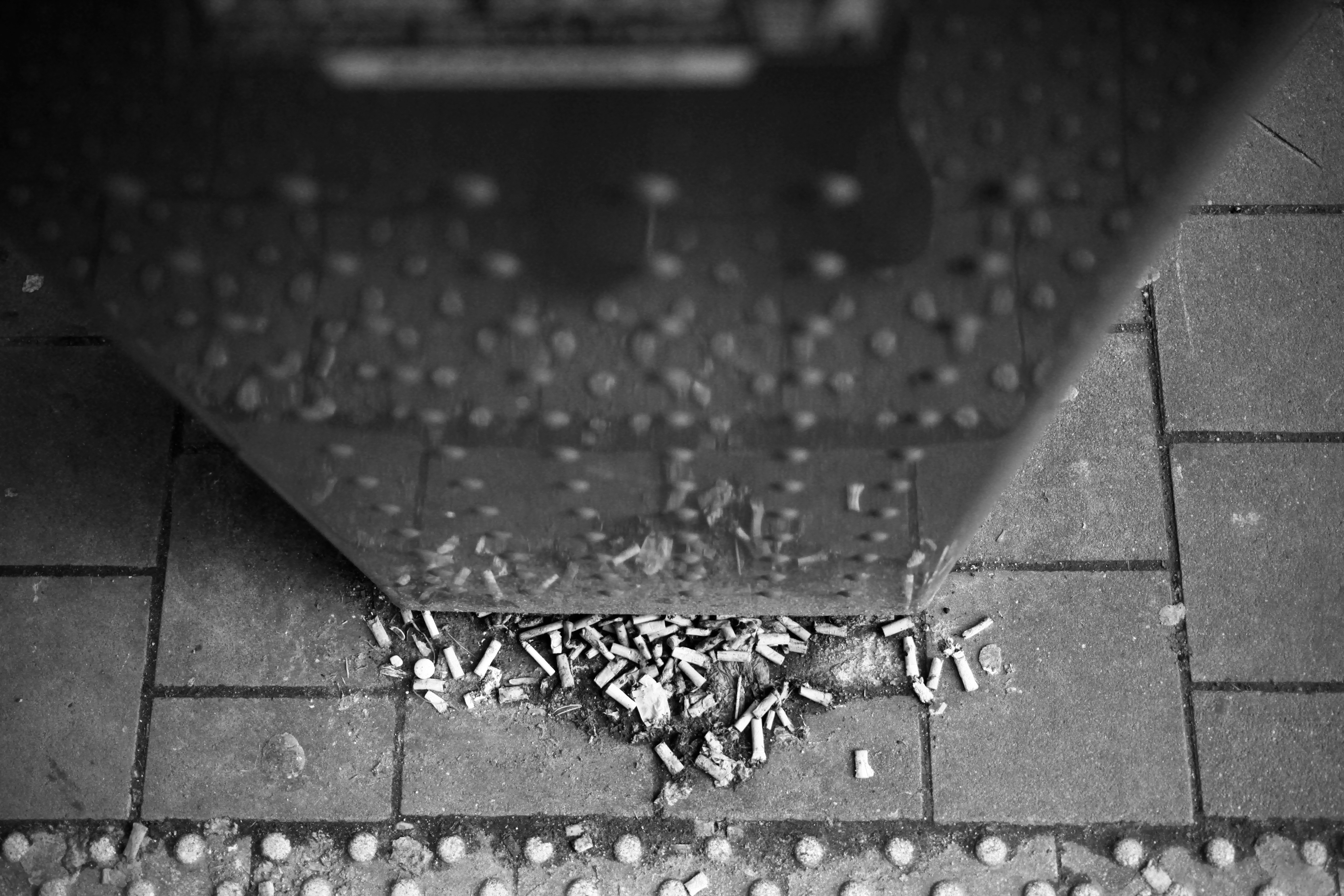 Cigarette butts litter the tiled ground near a structure.