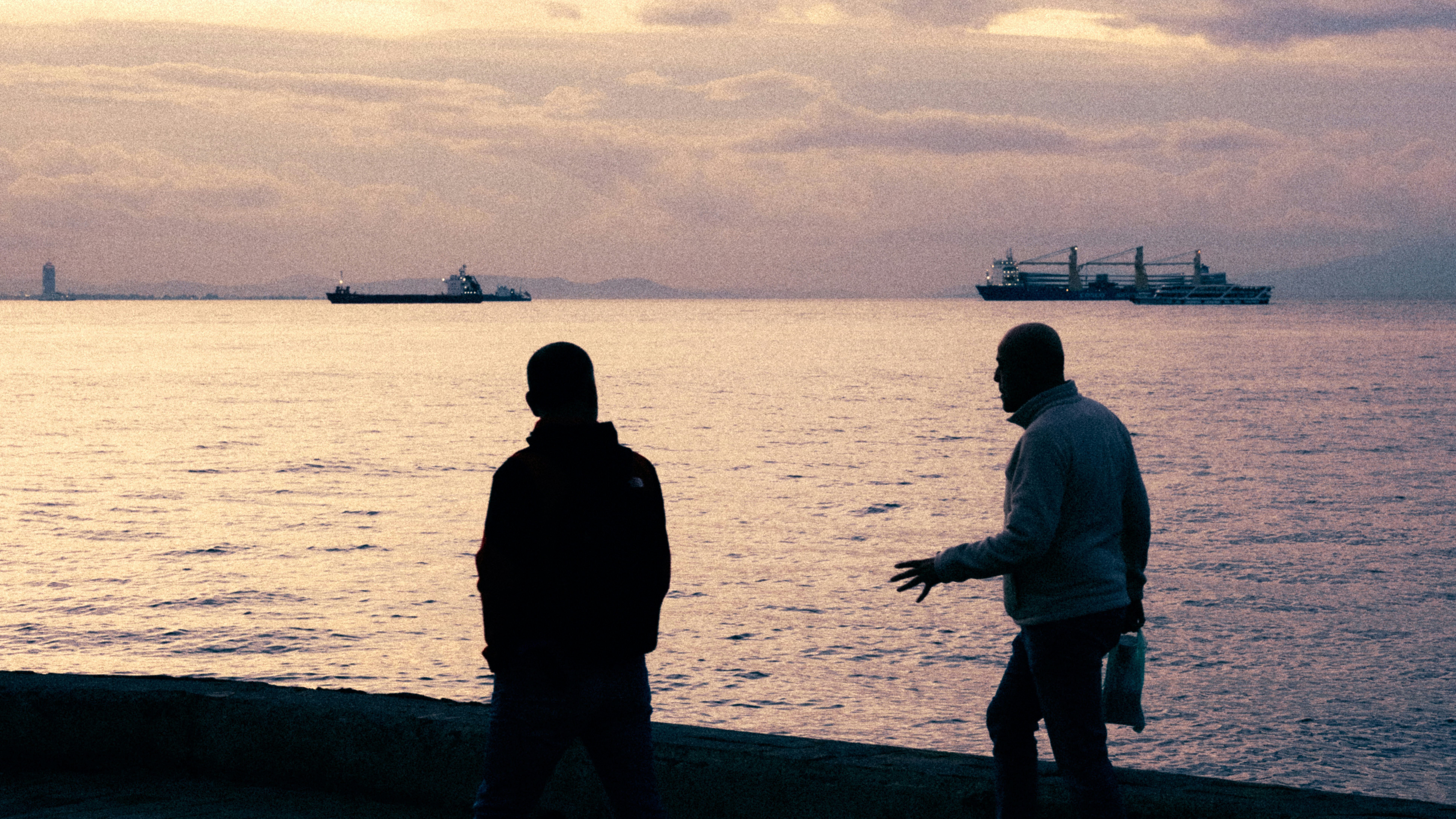 Two men walk by the water at sunset.