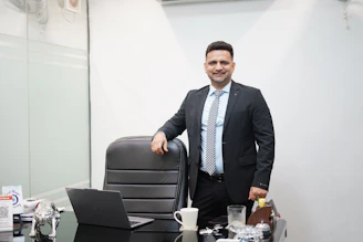 A man in a suit stands behind an office desk.