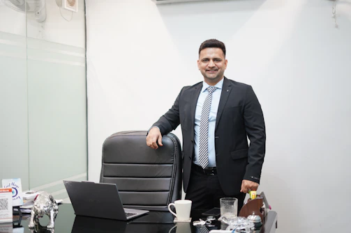 A man in a suit stands behind an office desk.