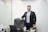A man in a suit stands behind an office desk.