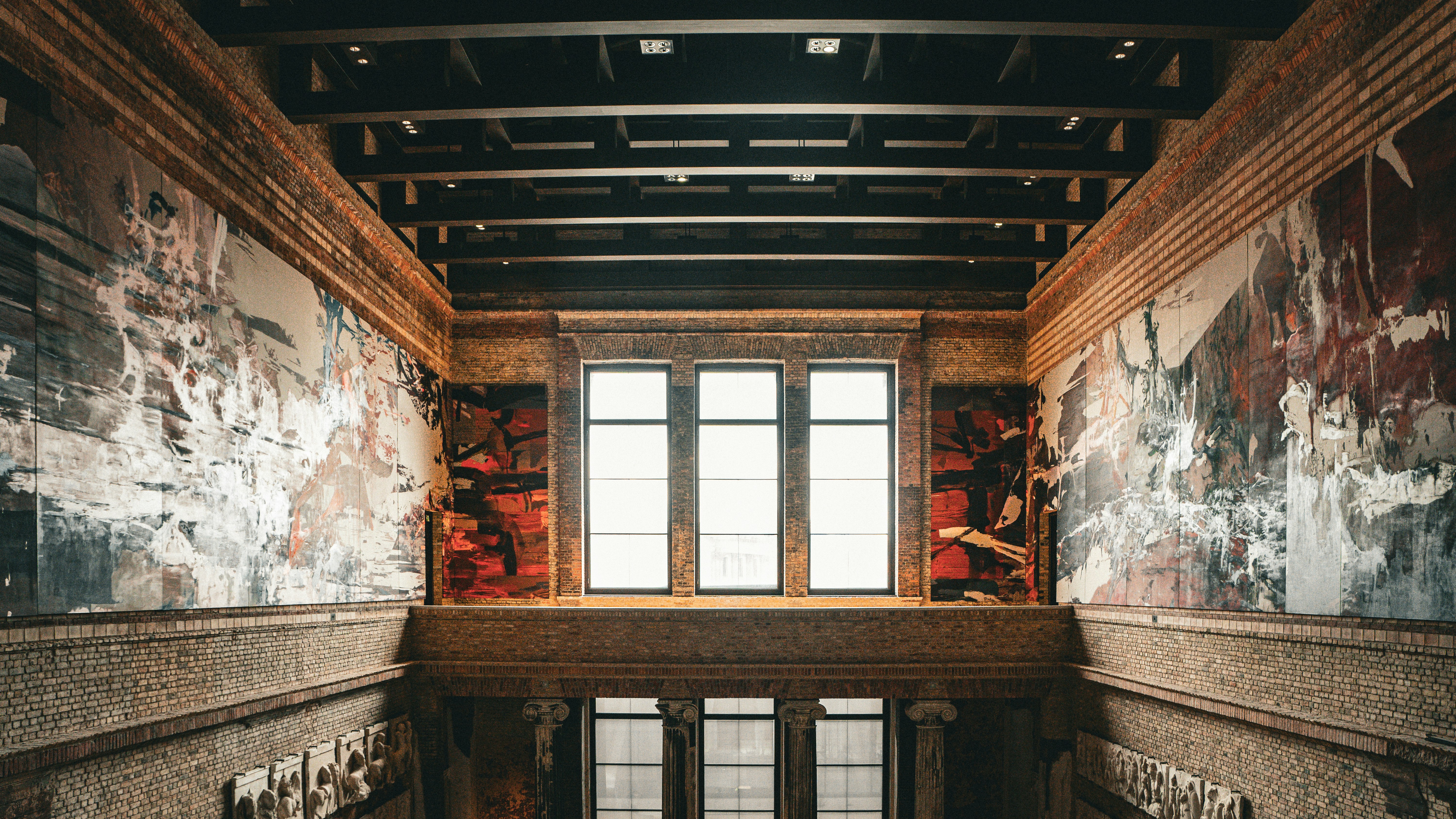 Interior of a grand building with large windows and murals.