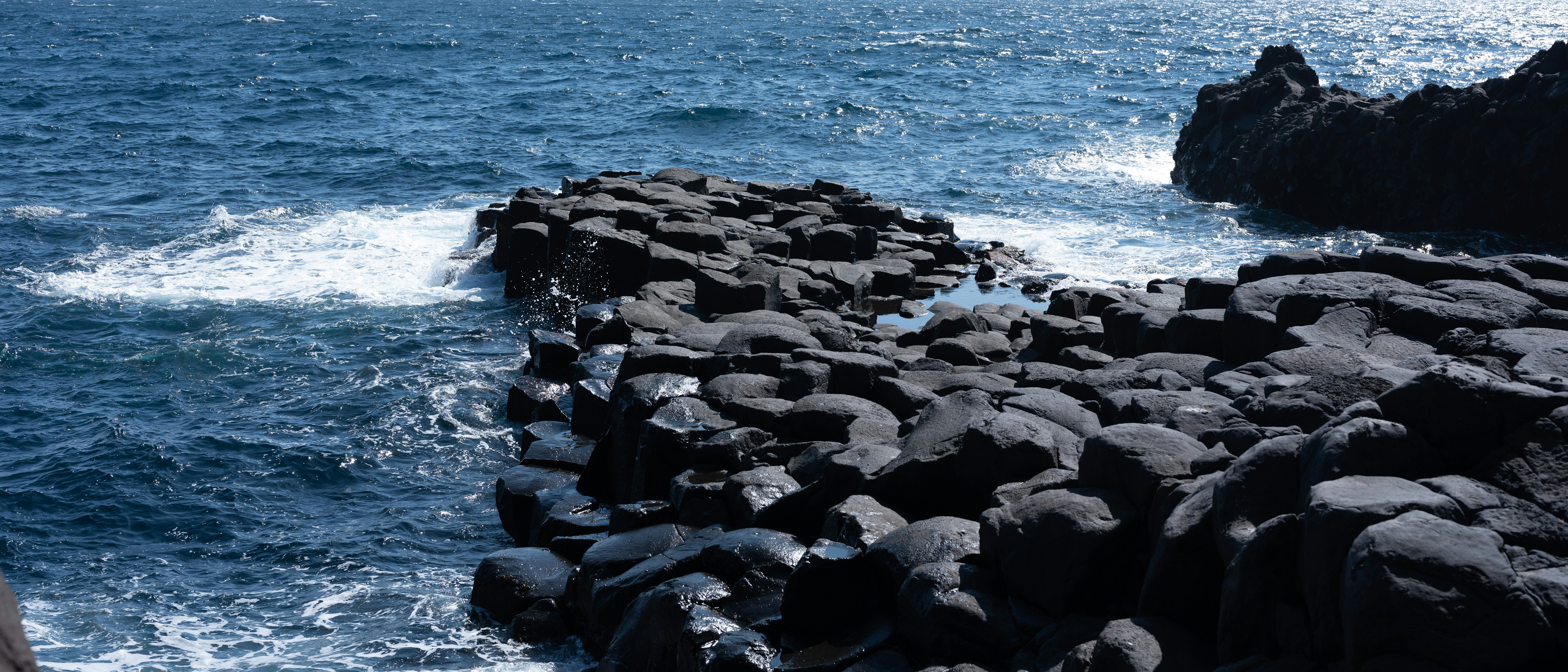 Waves crashing on dark volcanic rocks by the ocean.
