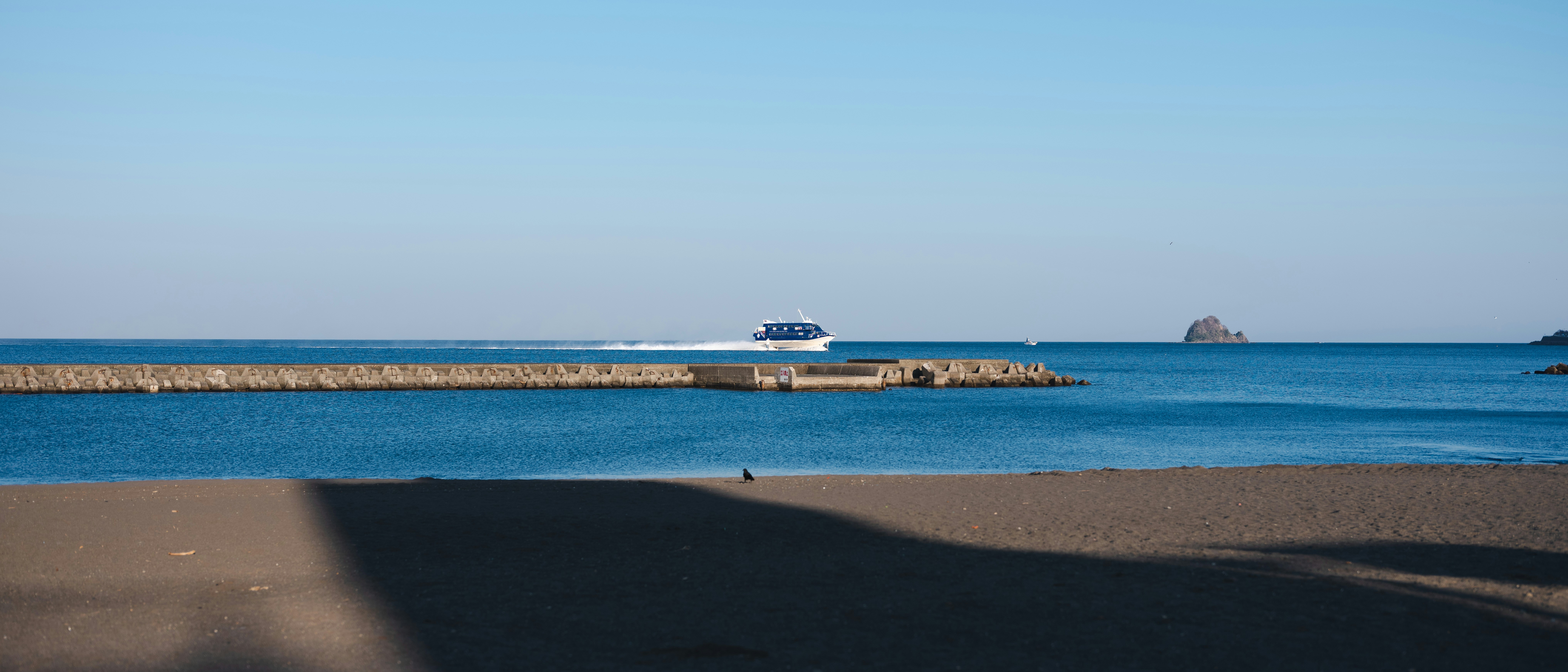 A ship sails on the blue ocean near a breakwater.
