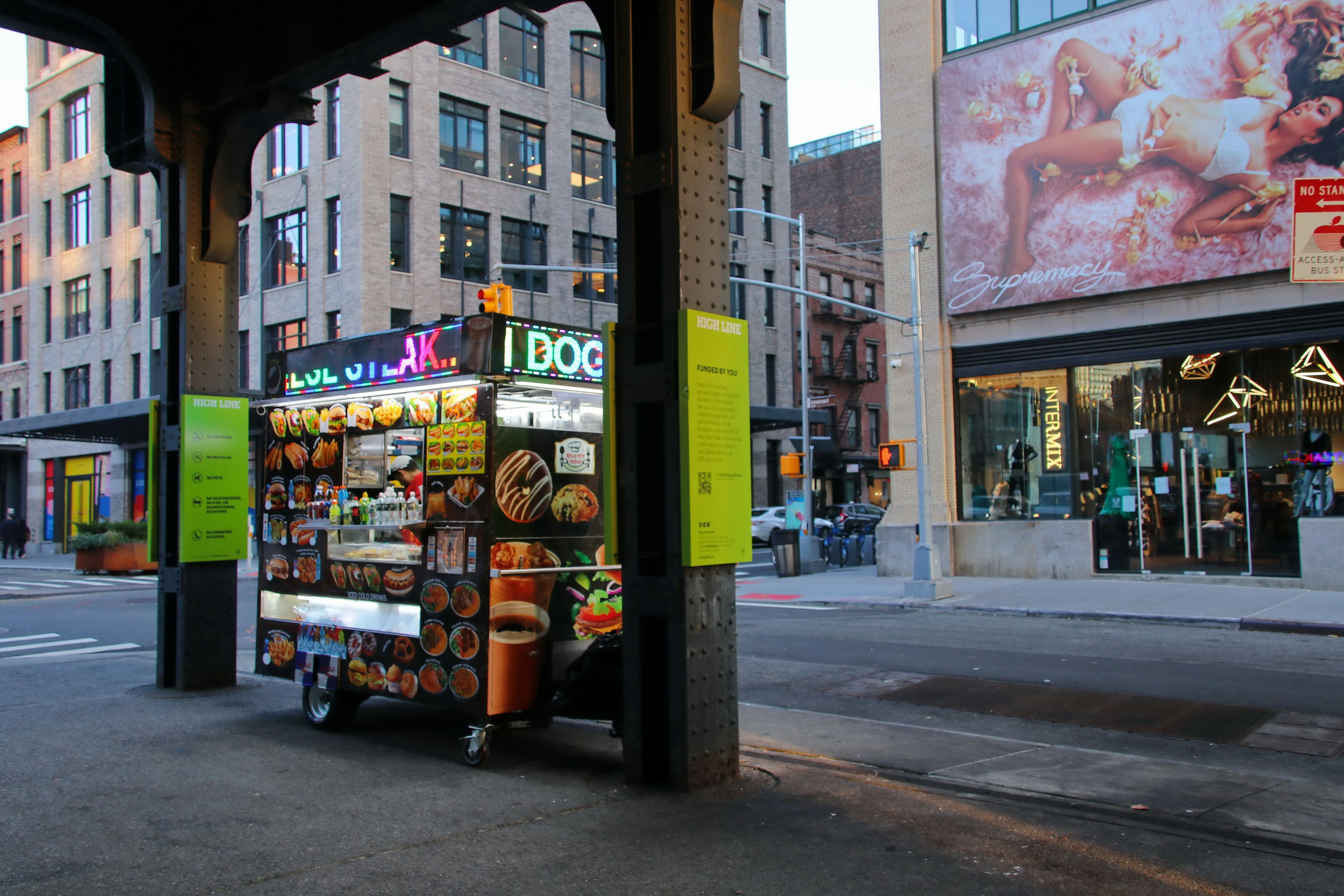 A new york city hot dog cart on a street.