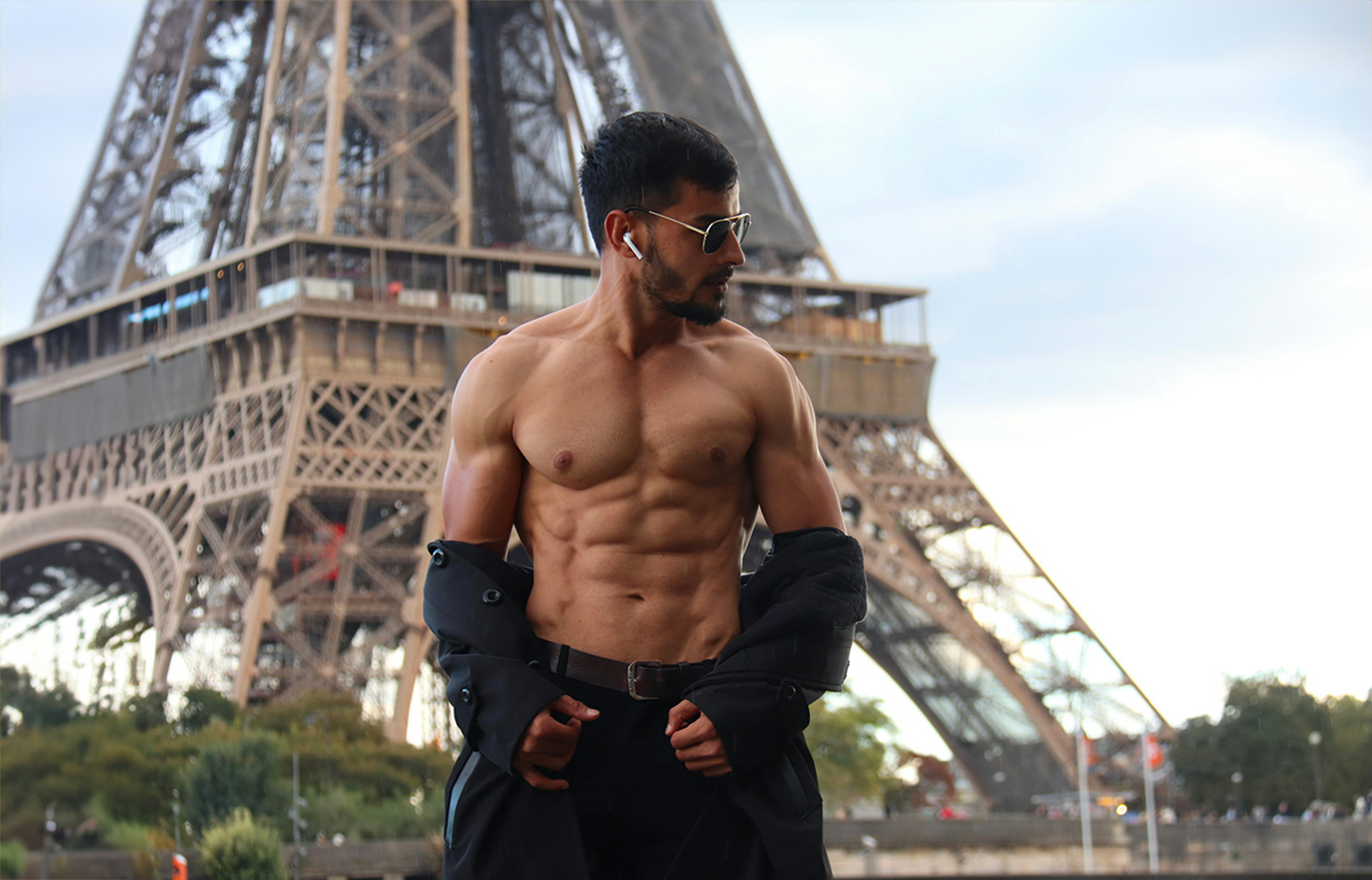 Muscular man posing in front of the eiffel tower.