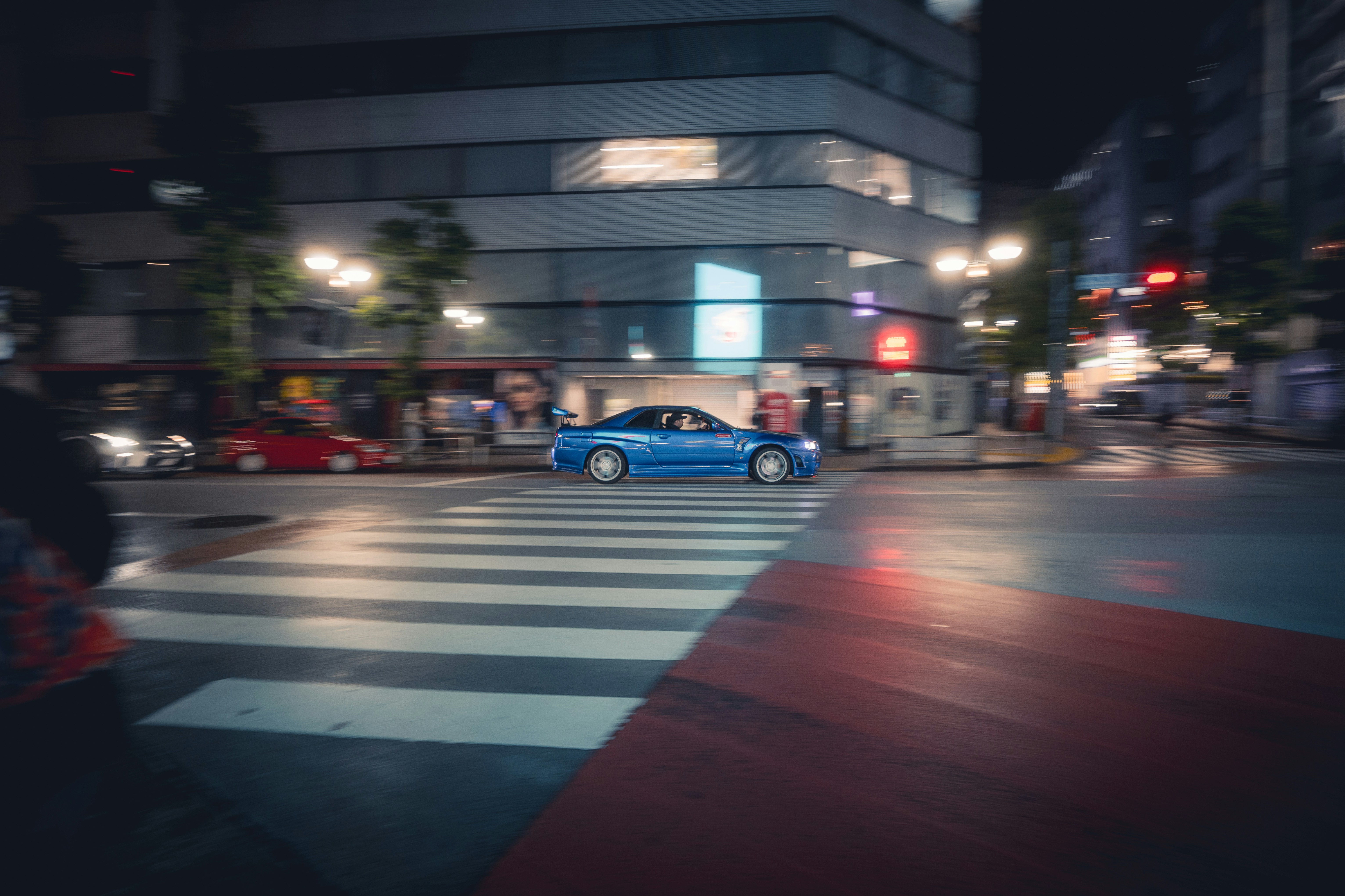 Um carro azul atravessa uma faixa de pedestres à noite.