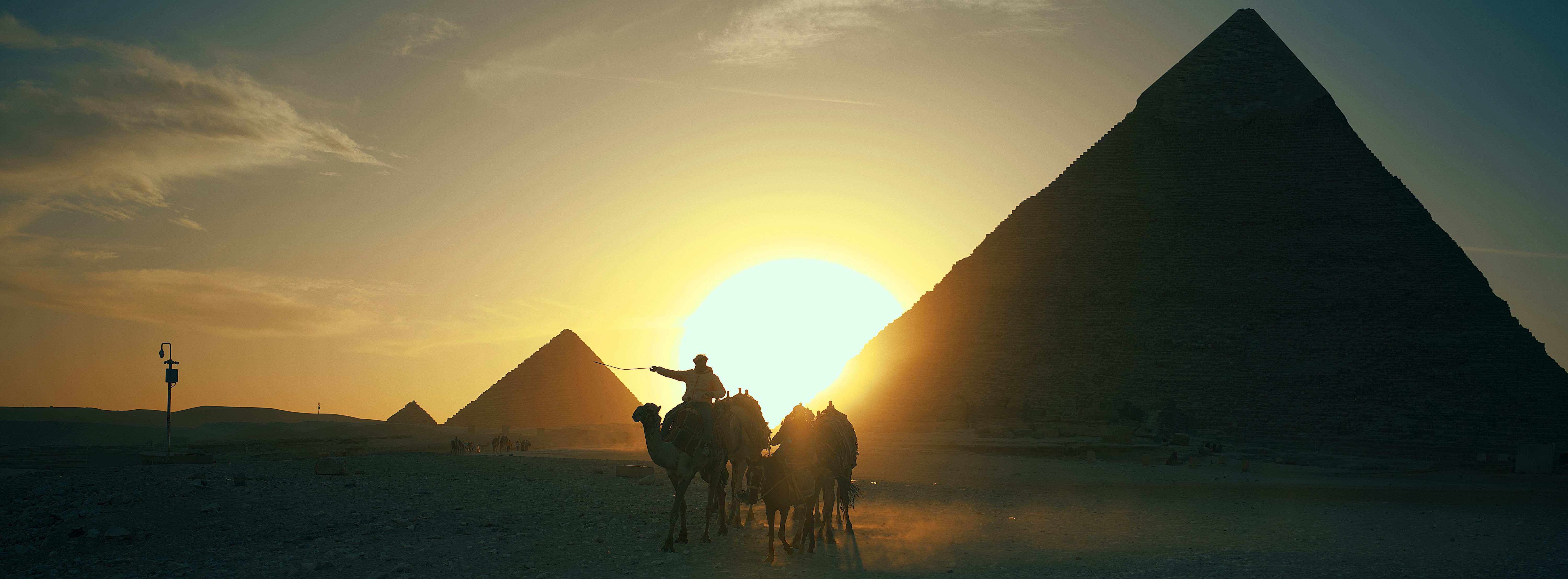 Camel caravan silhouetted against the pyramids at sunset