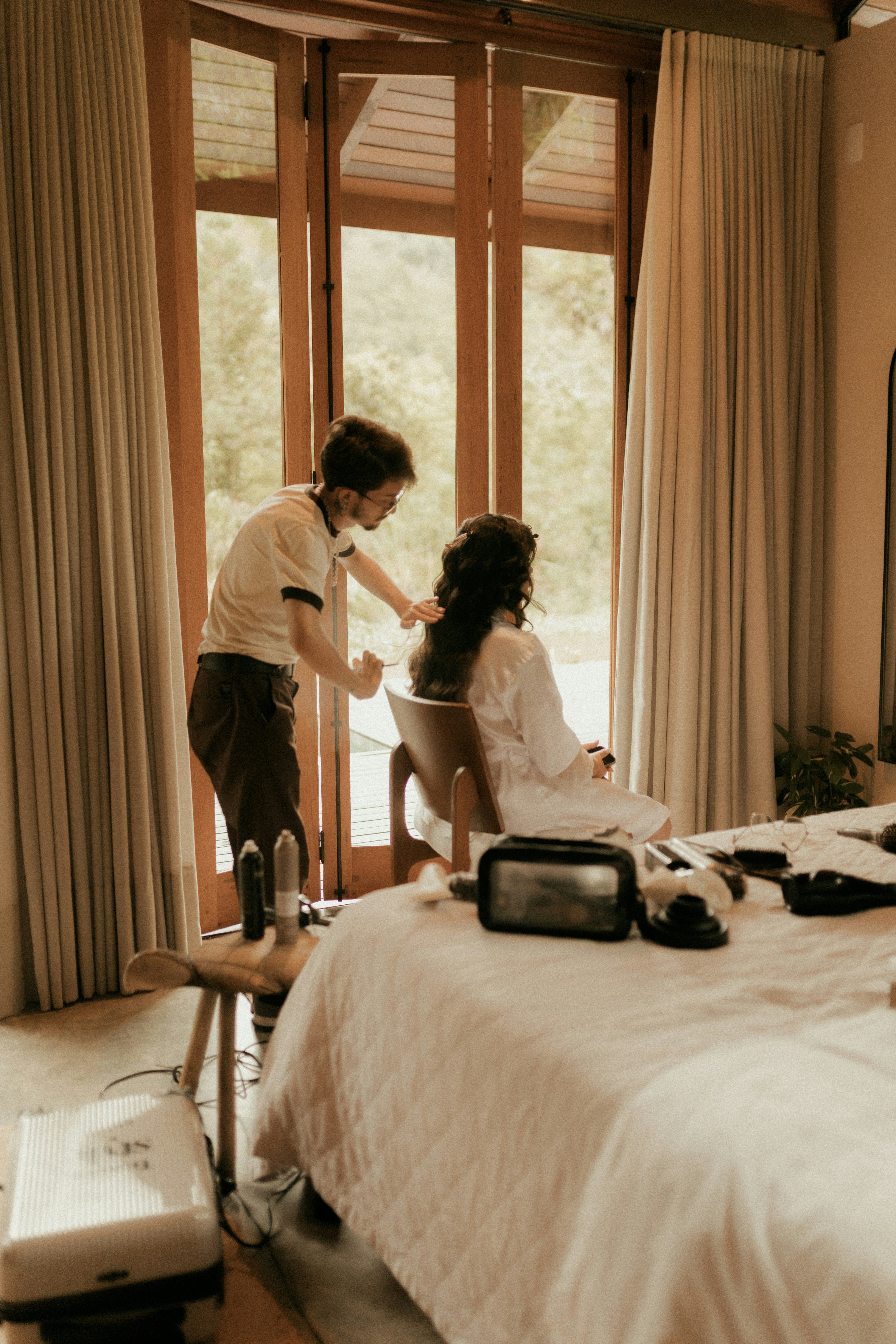 A stylist styles a woman's hair by the window.