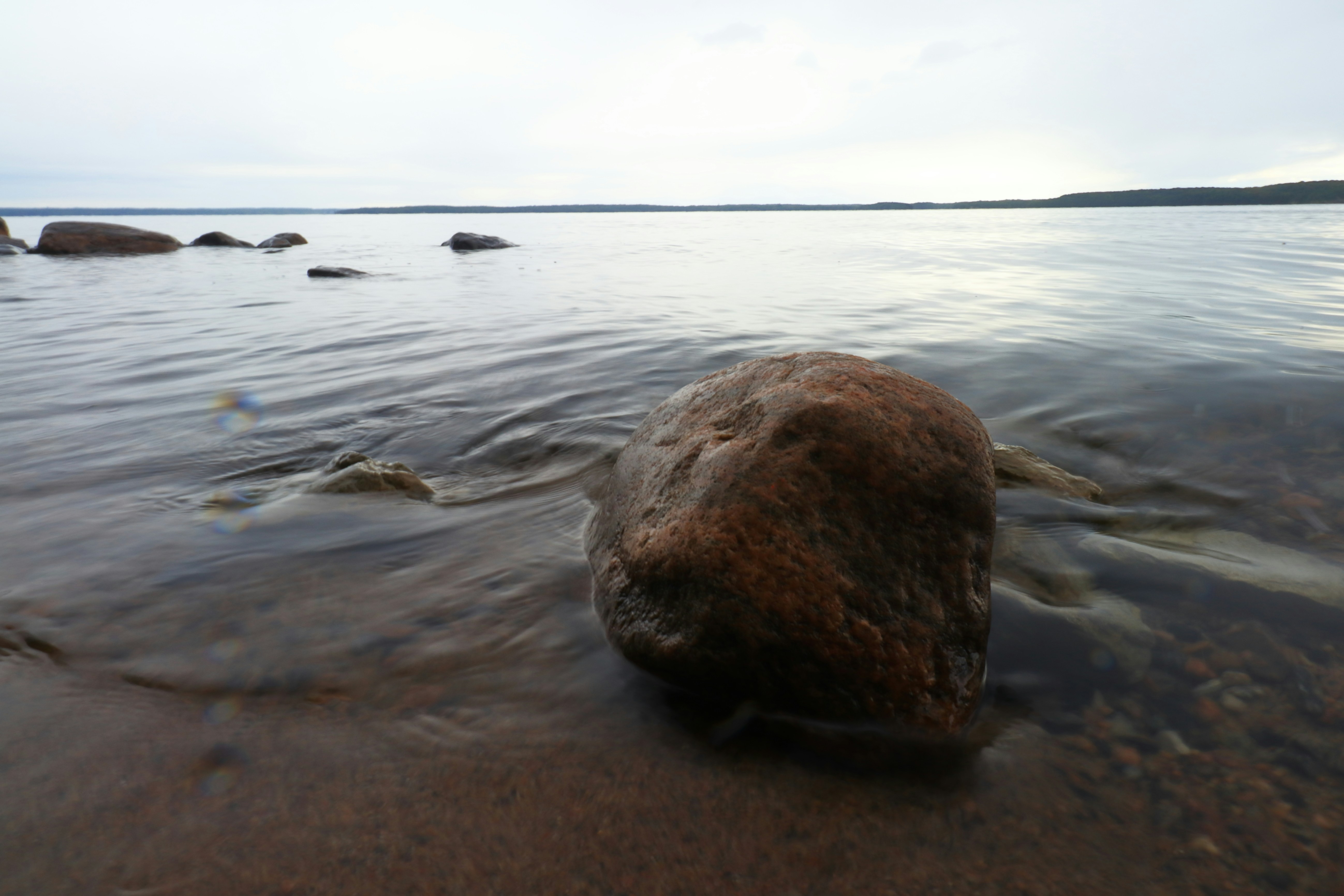 A large rock sits on a sandy shore near water.
