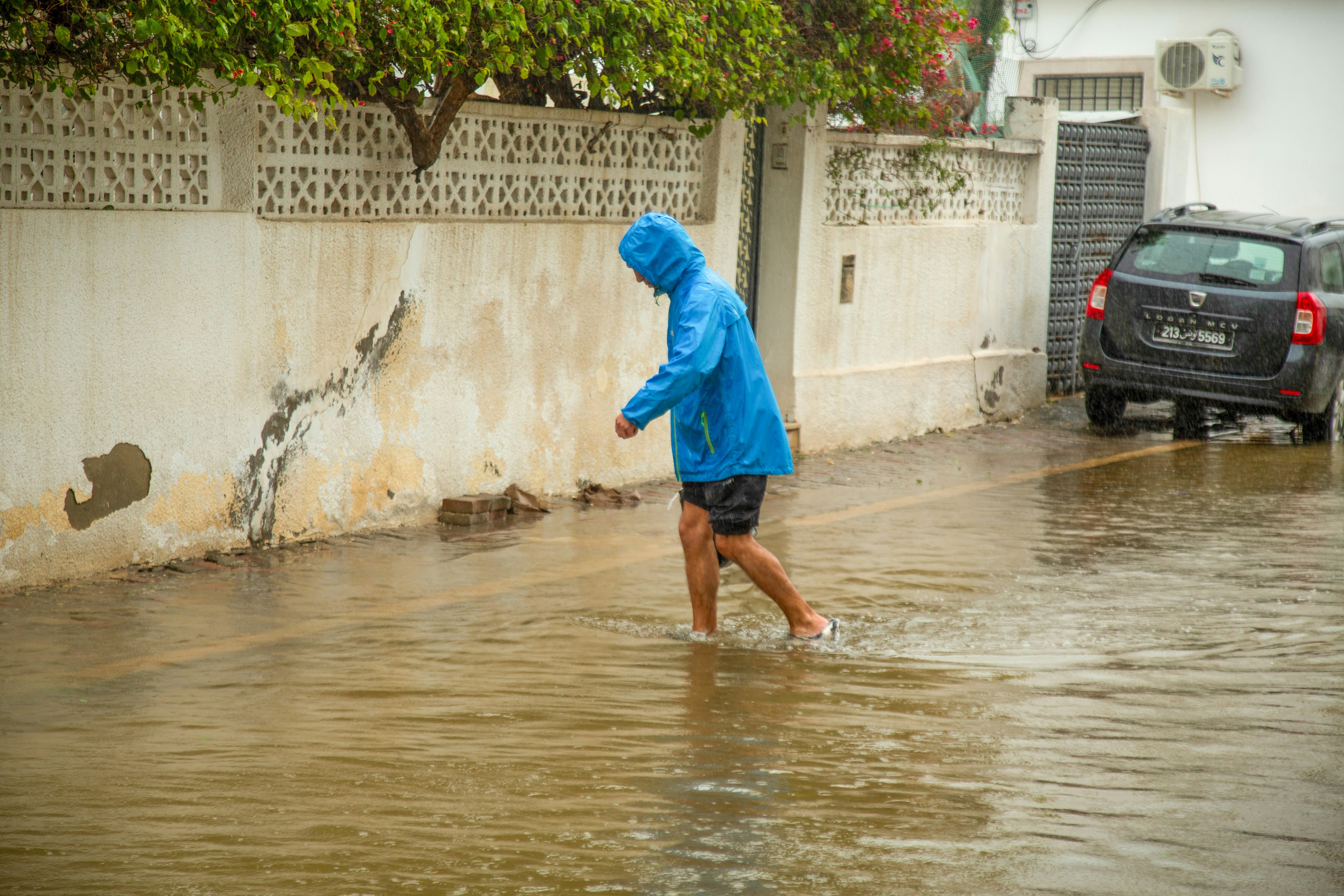 Person in blue raincoat walks through flooded street.
