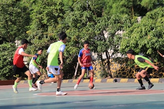 Boys playing soccer on a sunny outdoor court.